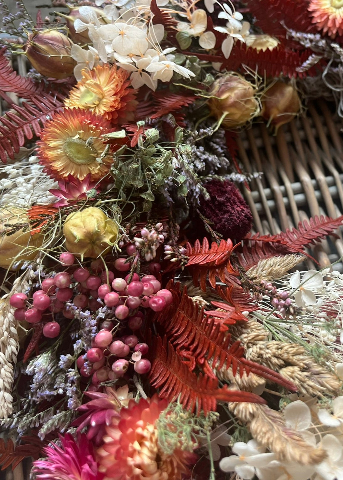 Close-up of a wreath made of dried flowers and leaves with a woven background.