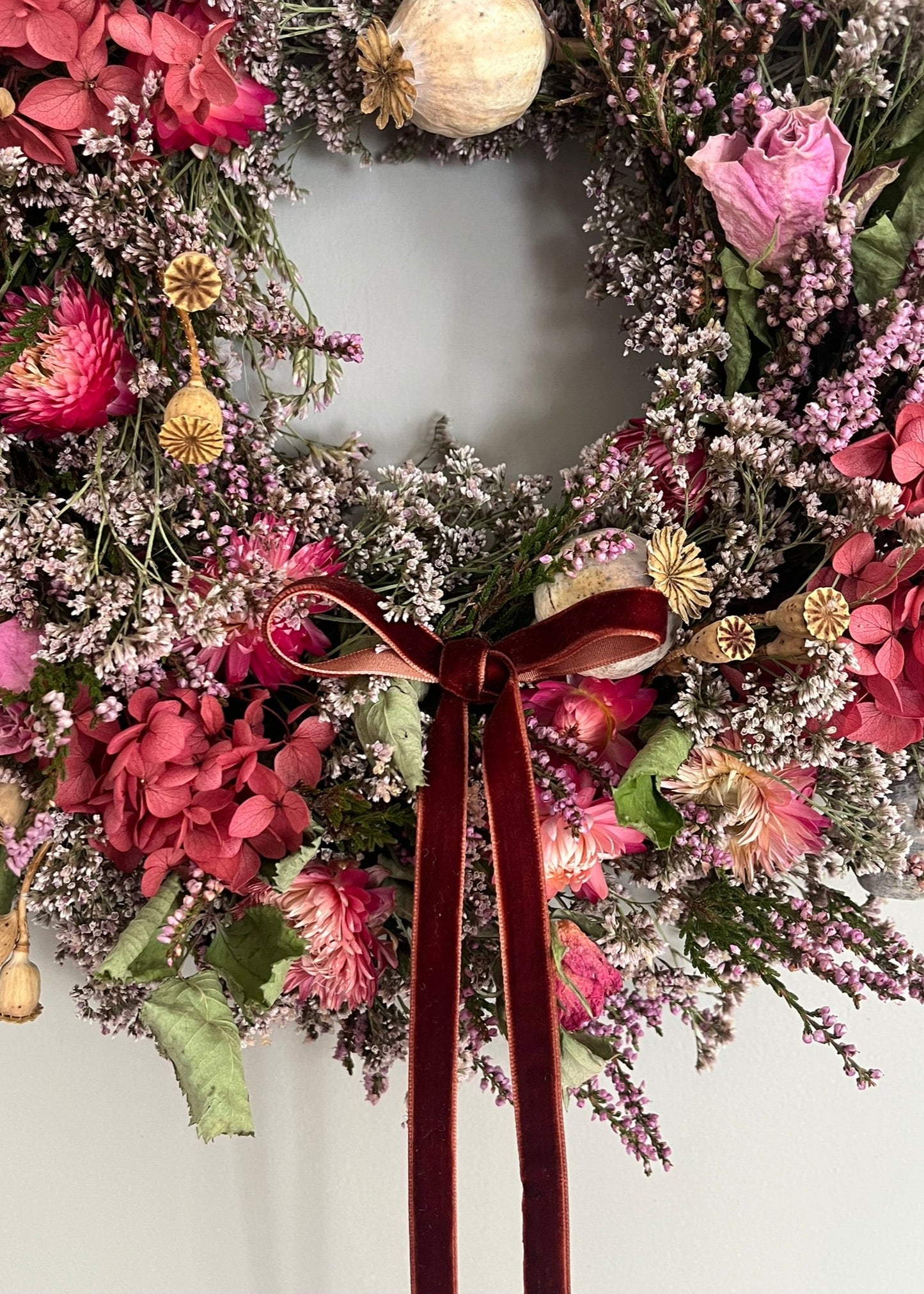 Floral wreath with pink and purple flowers and a brown ribbon on a white background