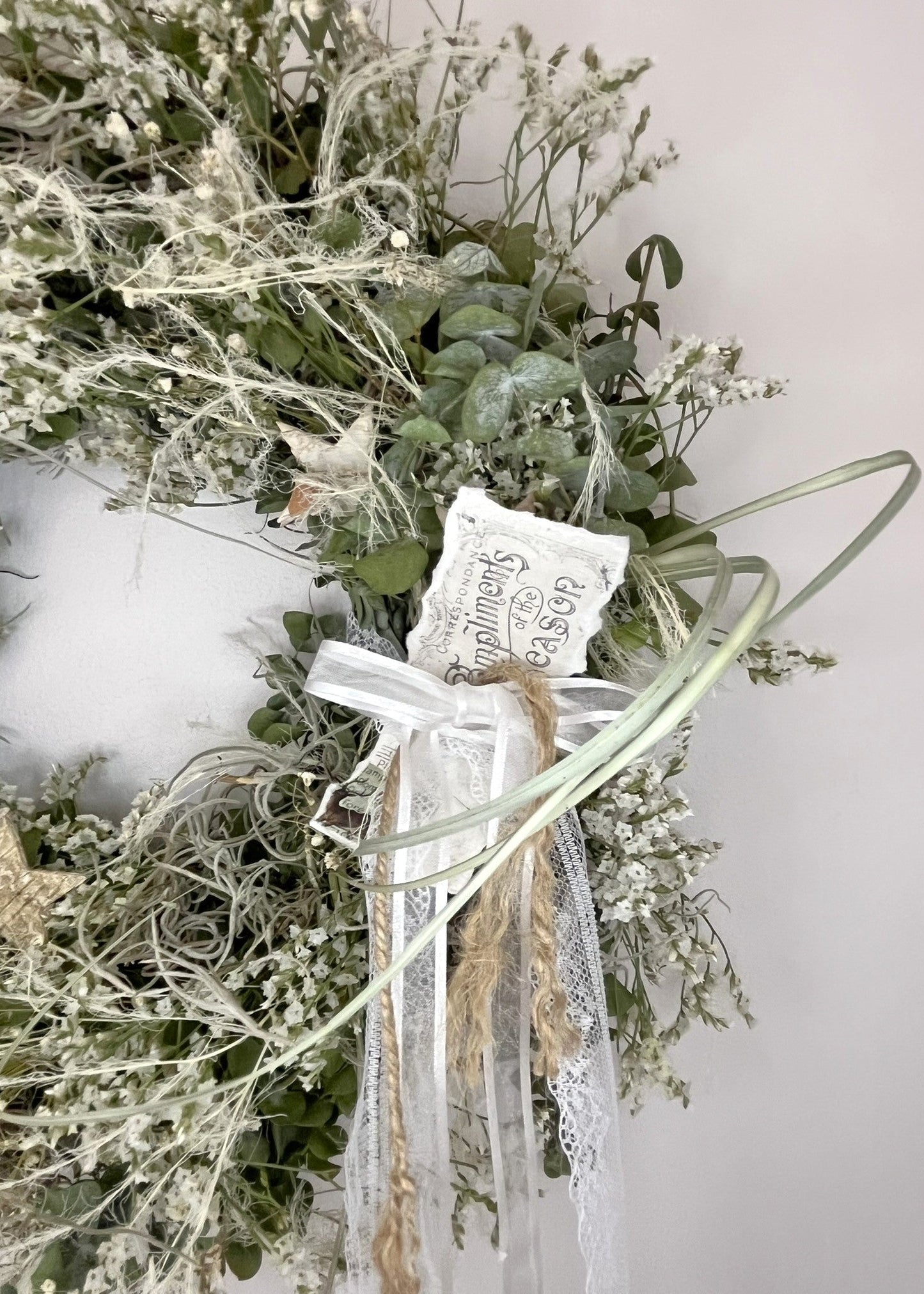 Decorative wreath with greenery, ribbons, and a small tag on a light background