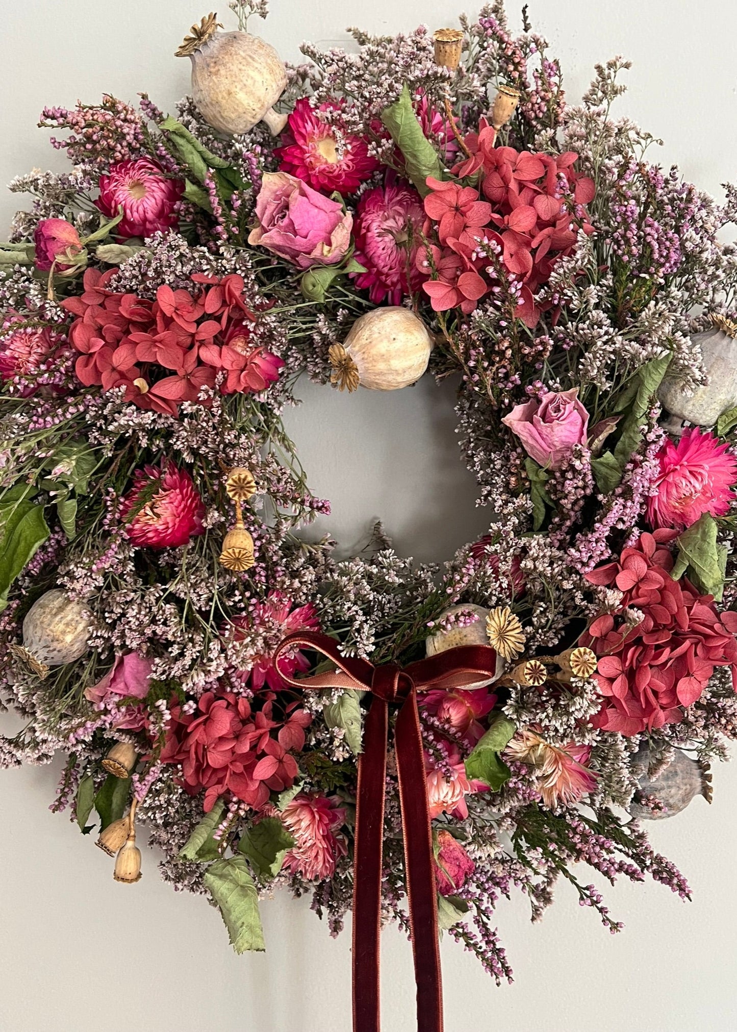 Floral wreath with pink flowers, gold ornaments, and a brown ribbon on a white background