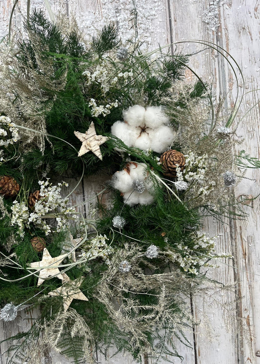 Decorative wreath with greenery, cotton, stars, and pinecones on a wooden surface