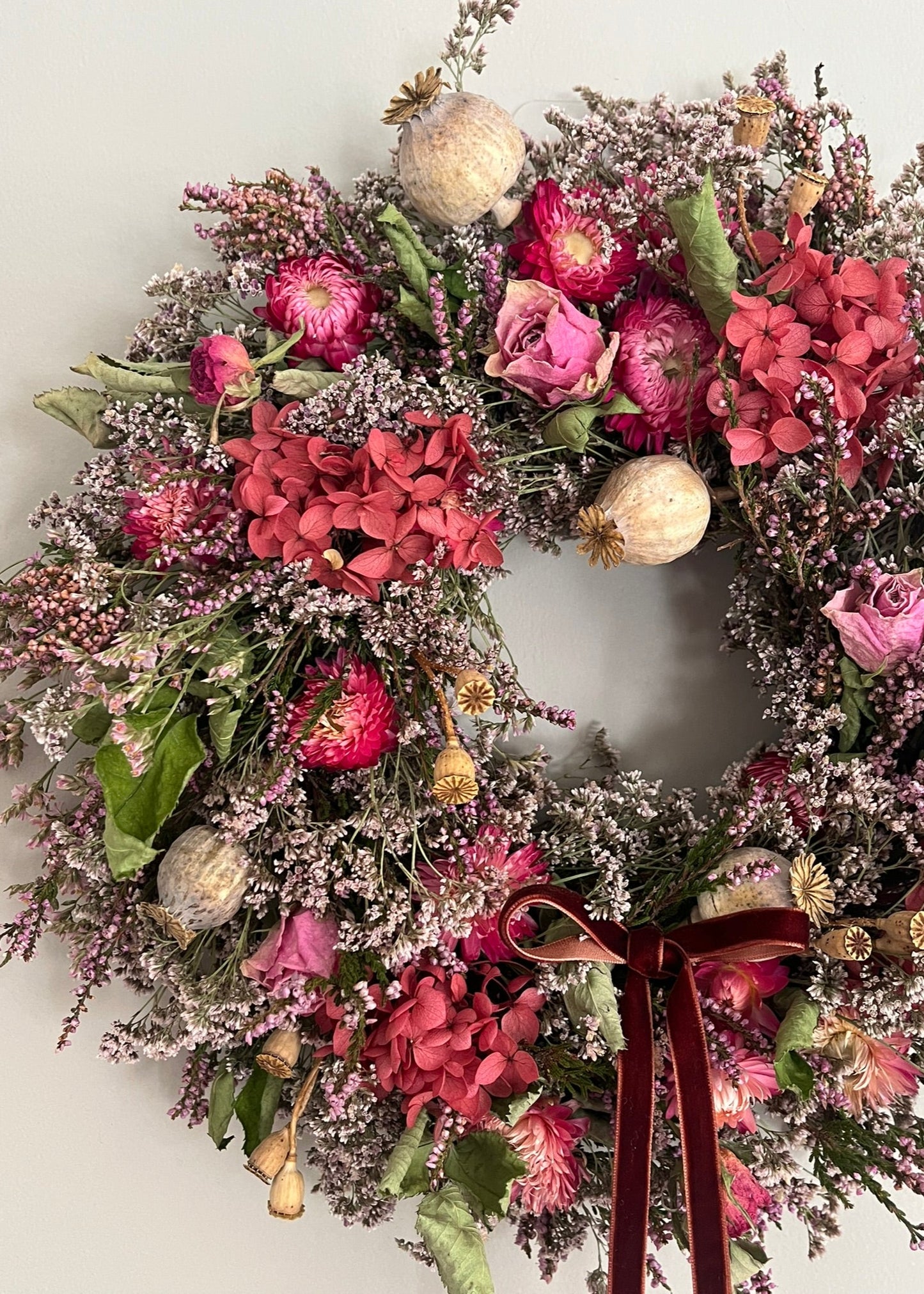 Floral wreath with pink and red flowers and a brown ribbon on a white background