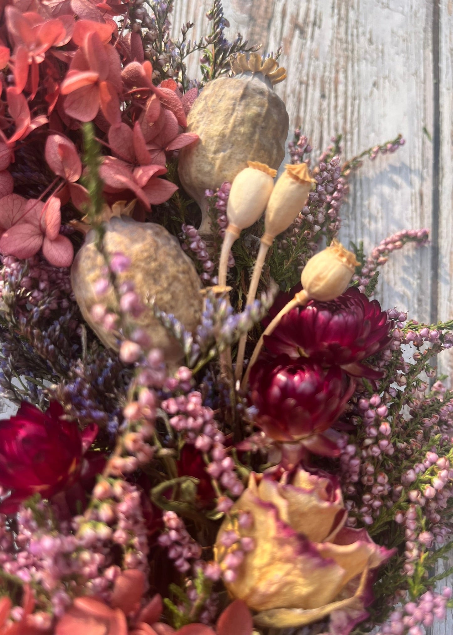 Bouquet of dried flowers with red, pink, and purple hues against a wooden background