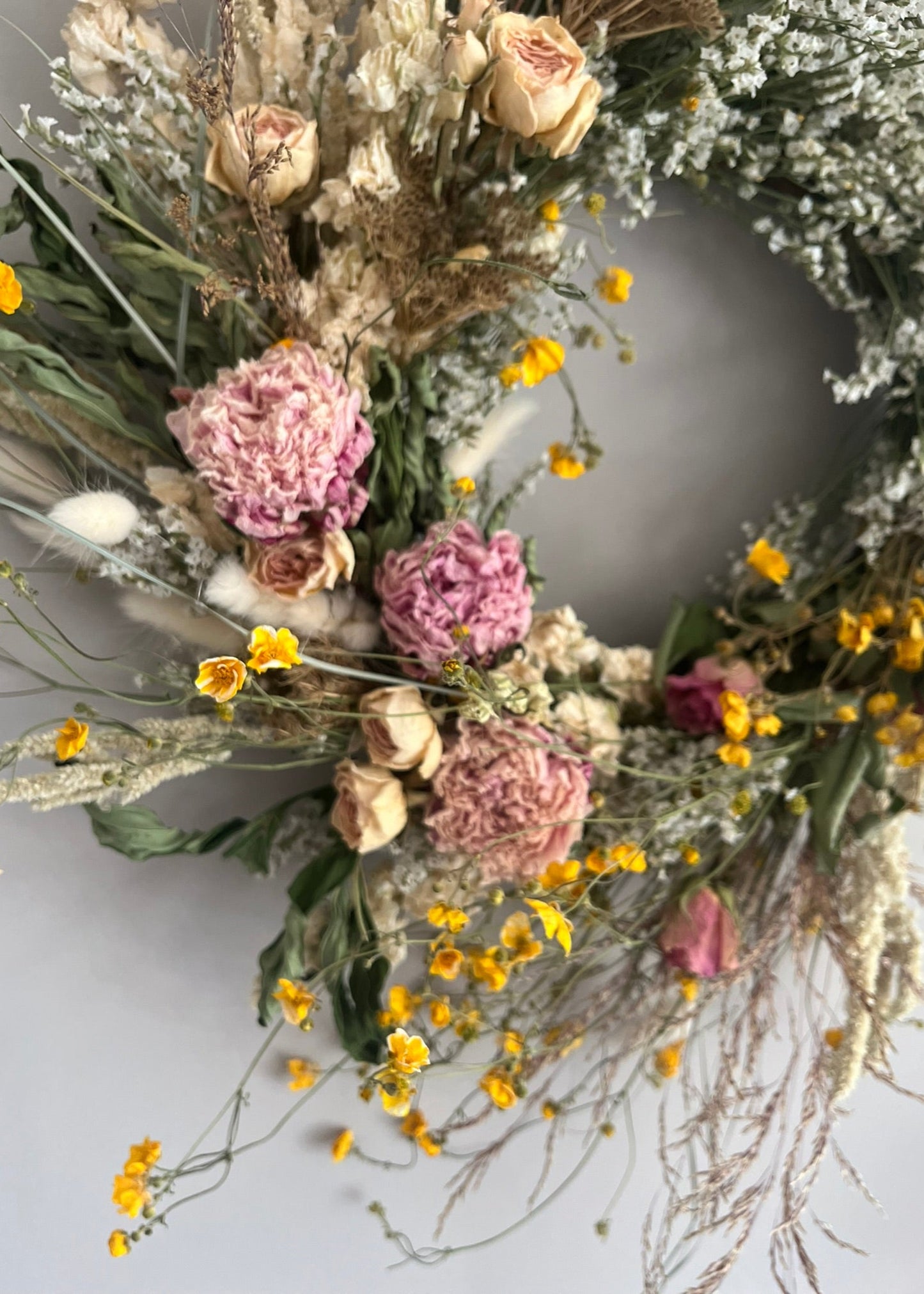 Dried flower wreath with pink, yellow, and green flowers on a light gray background