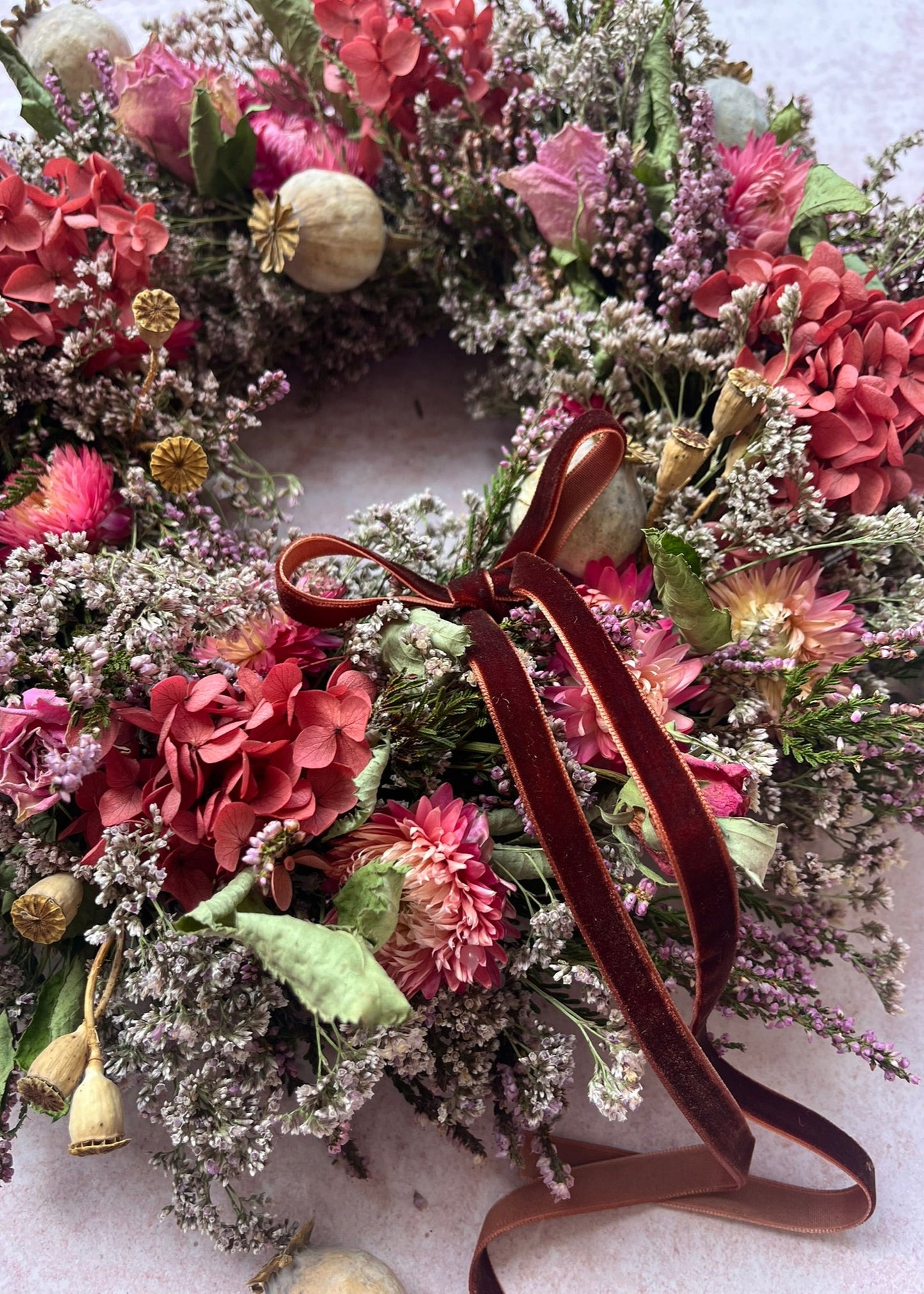 Floral wreath with pink and green flowers and a brown ribbon on a light background