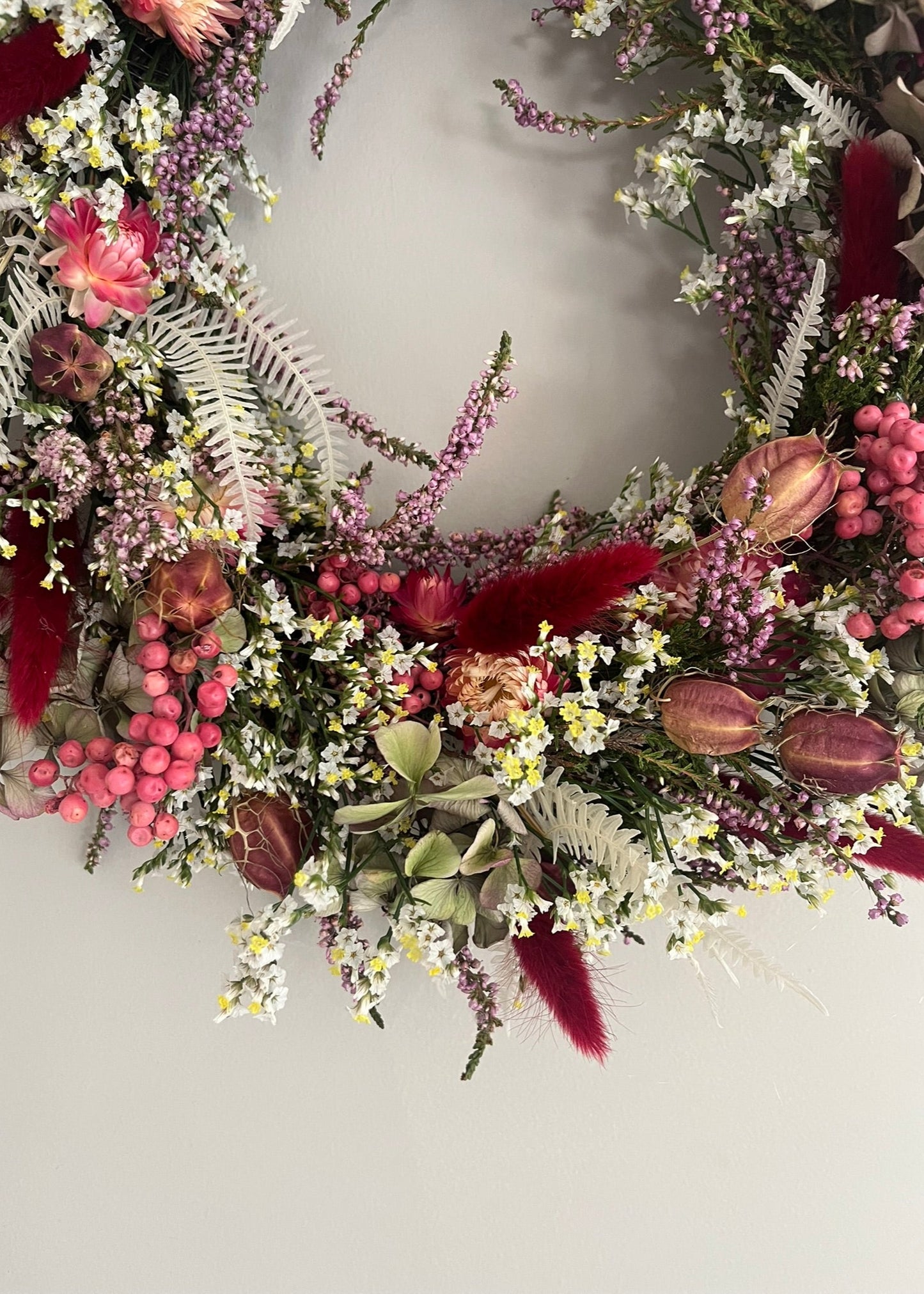 Decorative floral wreath with pink, red, and green flowers on a plain background