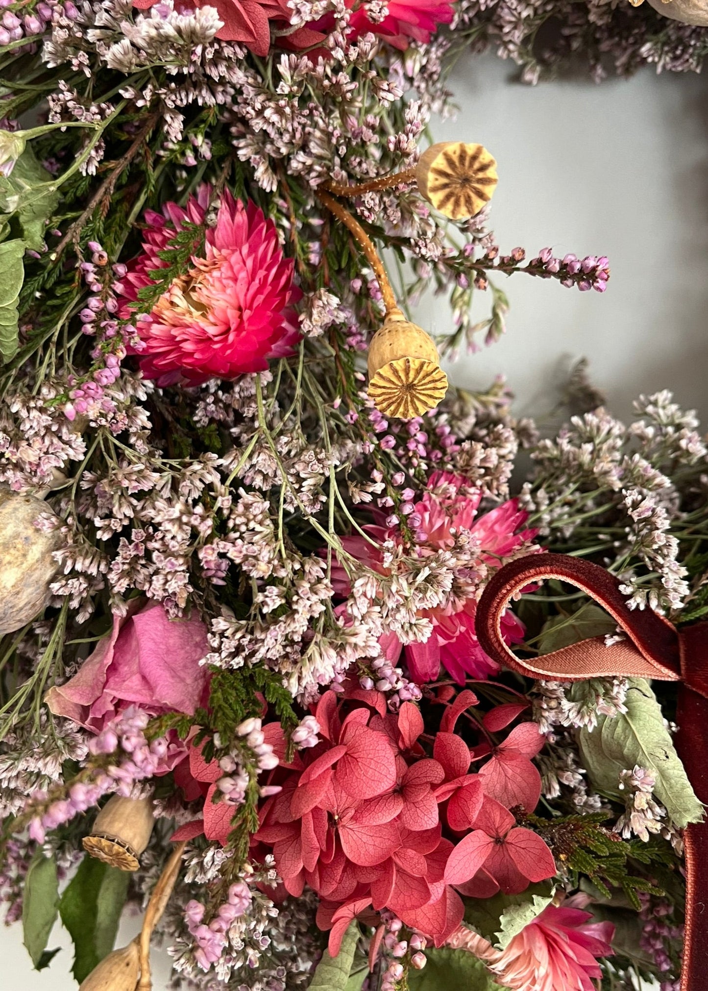 Decorative wreath with pink flowers, green leaves, and a brown ribbon on a white background