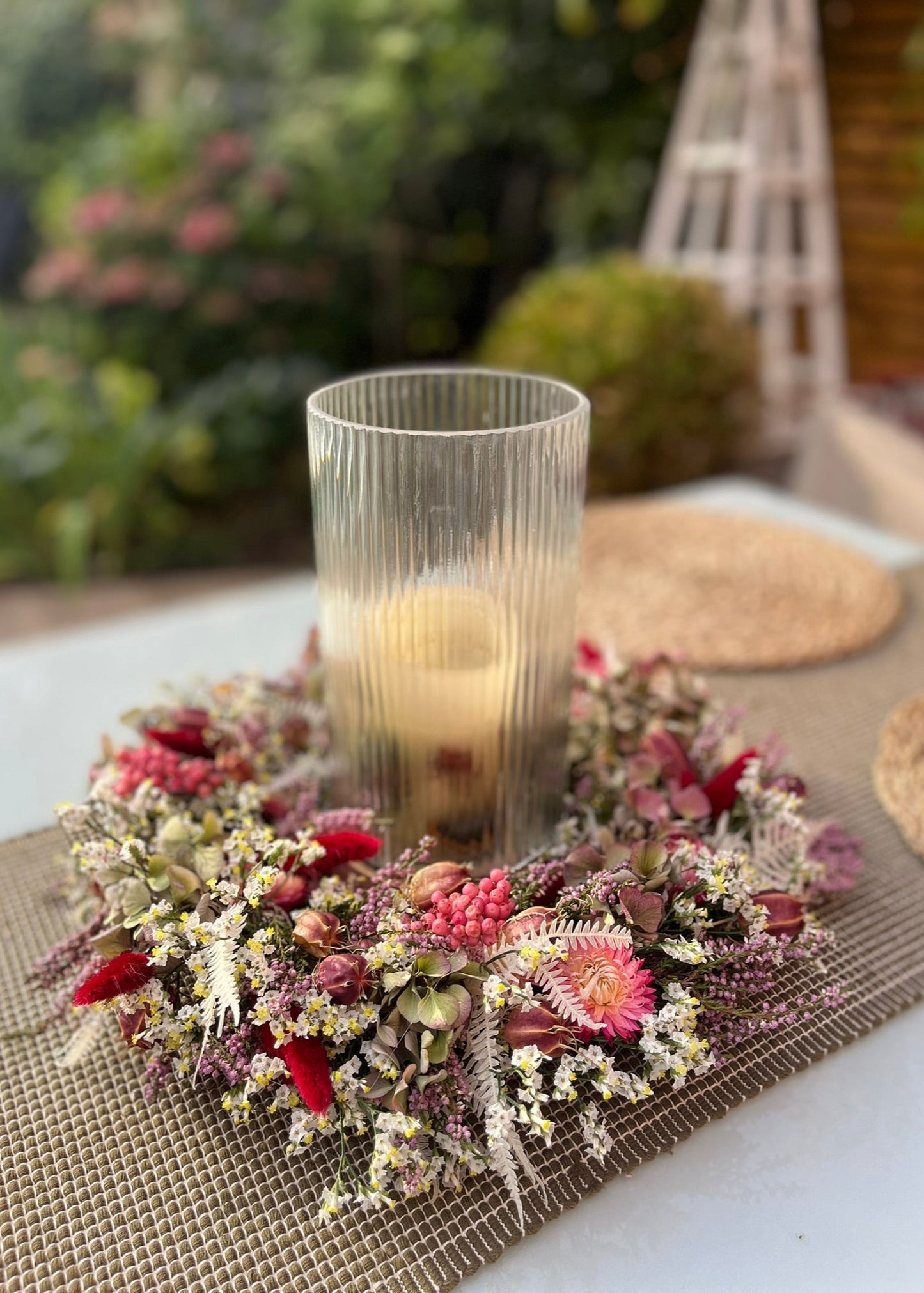 Decorative floral arrangement with a candle on a textured surface outdoors.