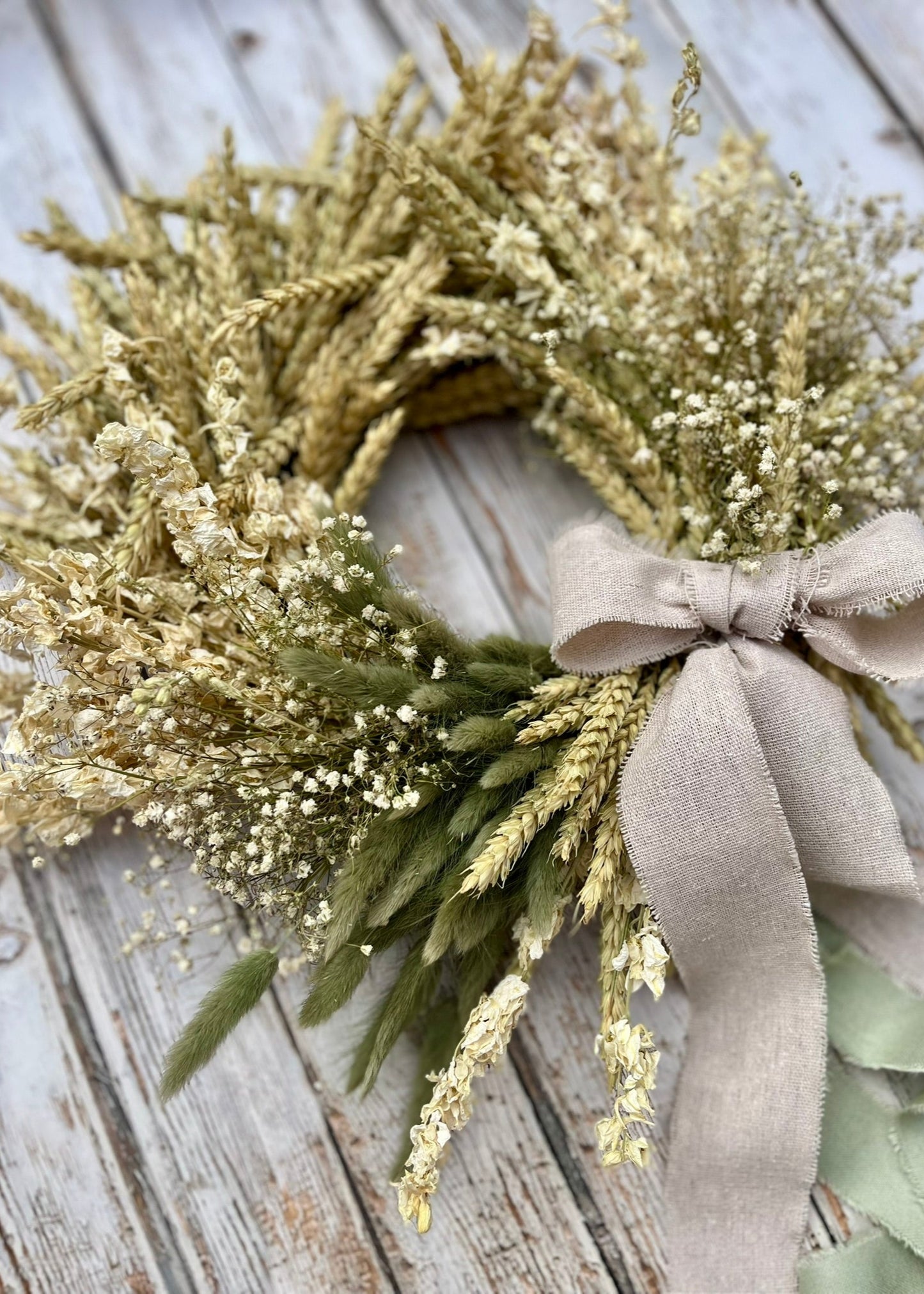 Wreath with greenery and a beige ribbon on a wooden surface