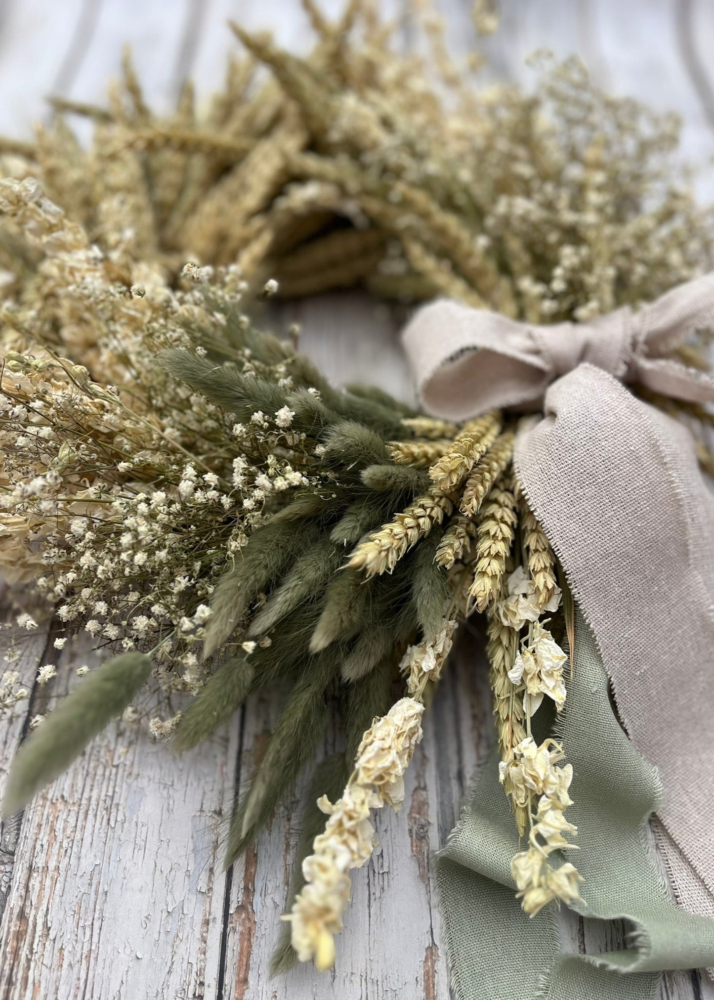 Wreath made of dried plants with ribbons on a wooden surface