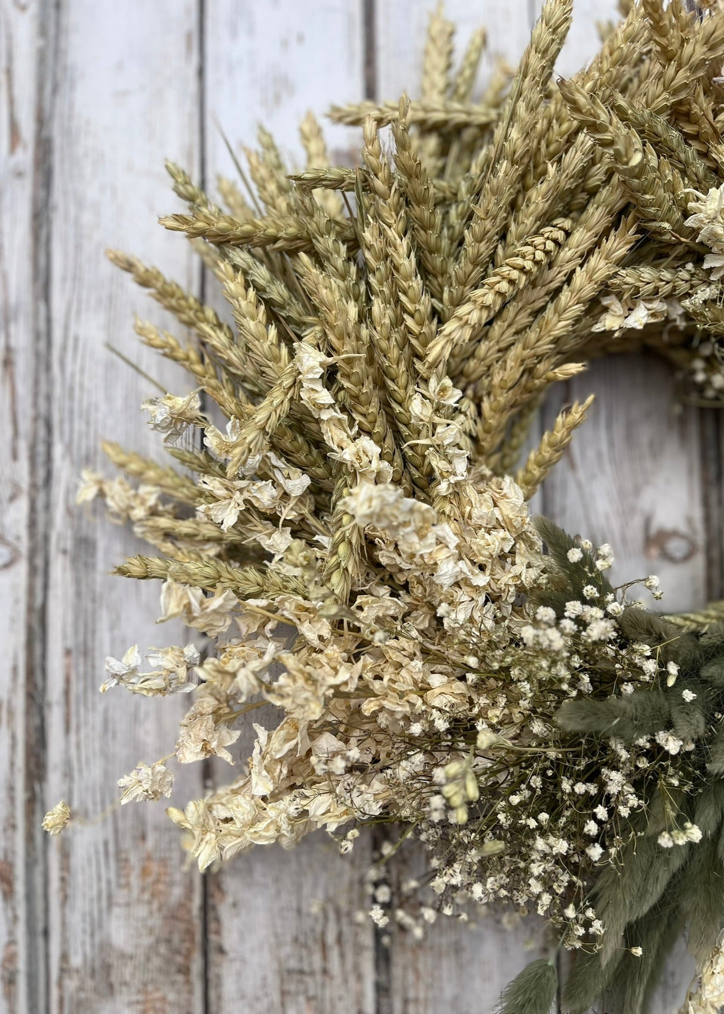 Wreath made of wheat and small white flowers on a wooden background
