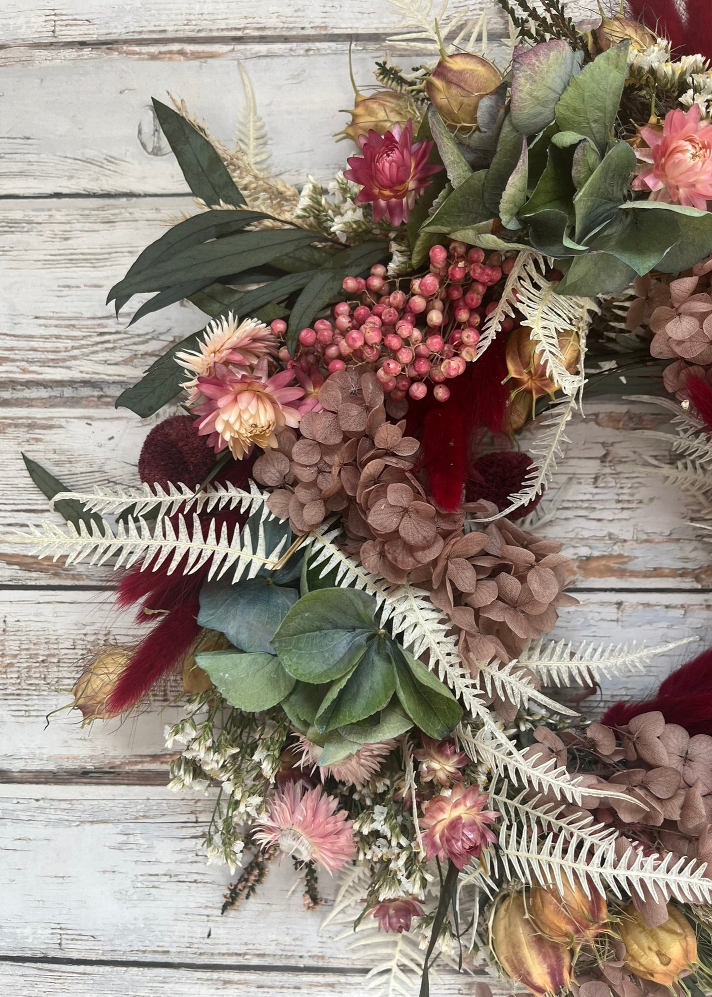 Decorative wreath with various plants and flowers on a wooden surface