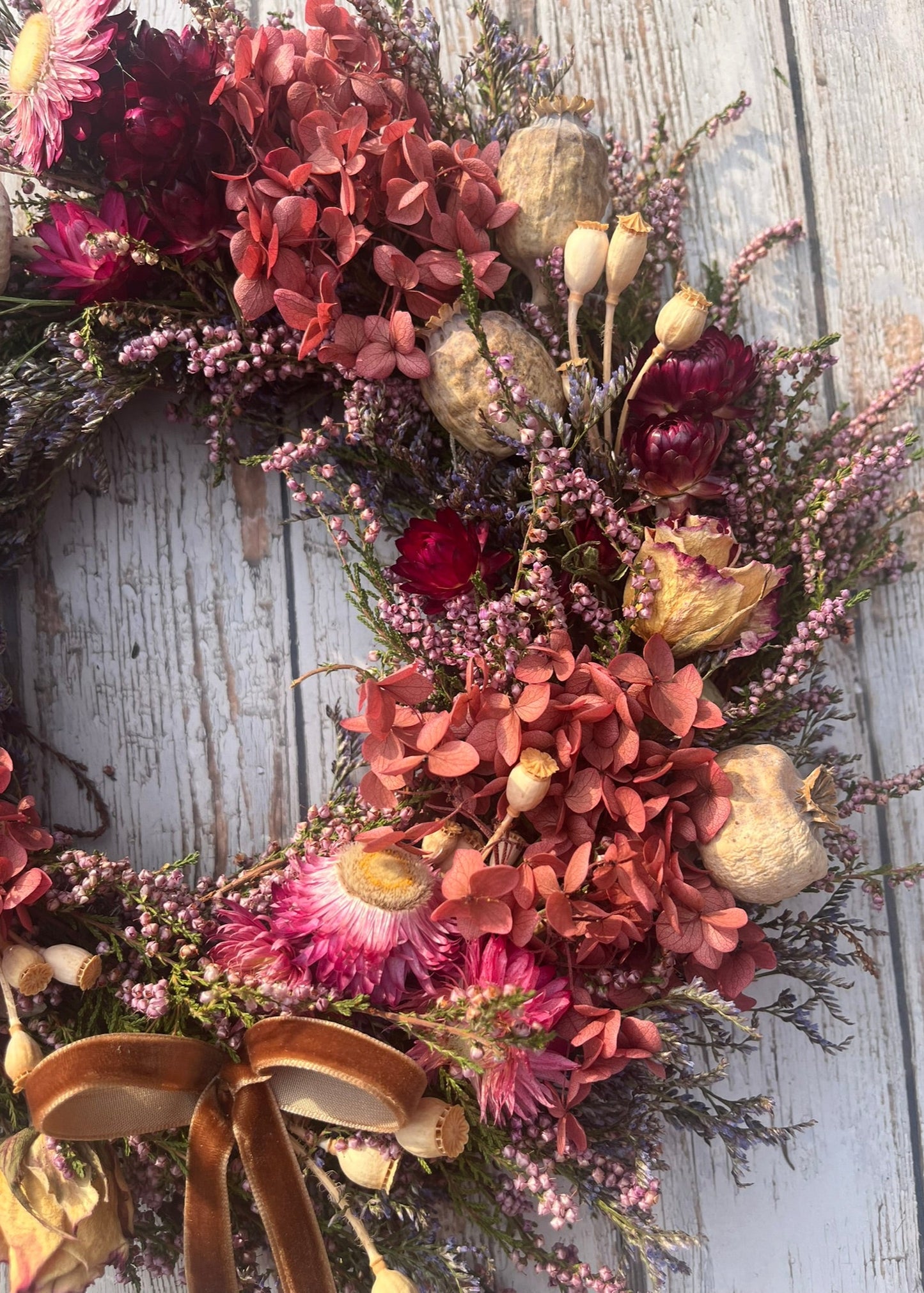 Floral wreath with dried flowers and a gold bow on a wooden background