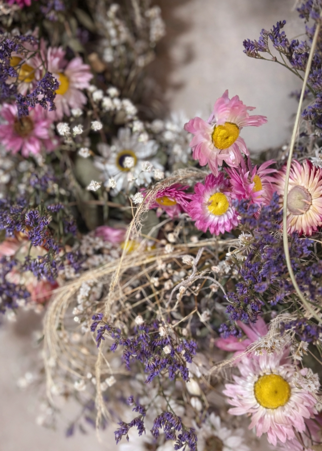 Pretty pastel spring wreath made with dried eucalyptus, white daisies and clusters of gypsophila in shades of pink and purple.