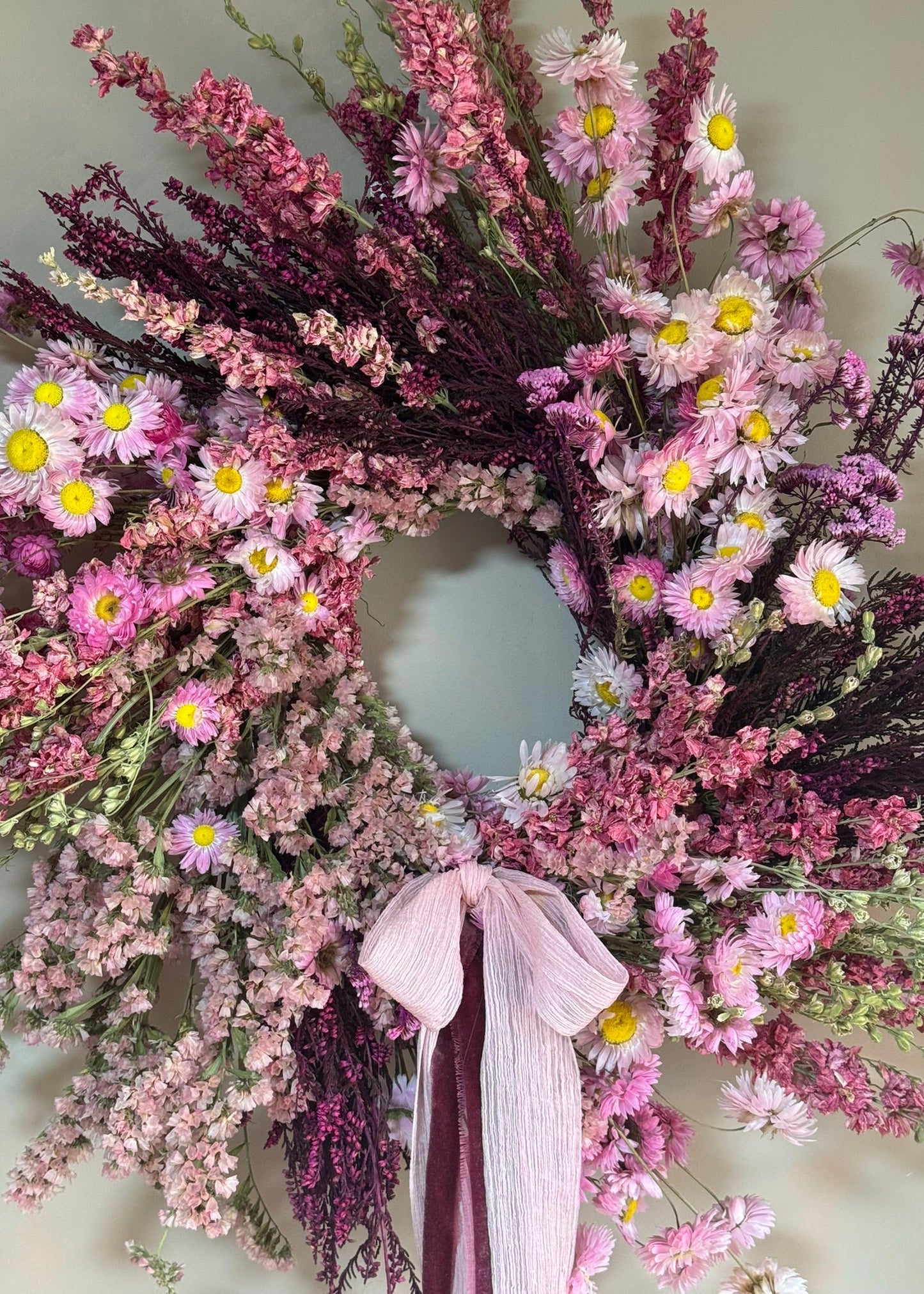 Floral wreath with pink and purple flowers and a white ribbon on a light background