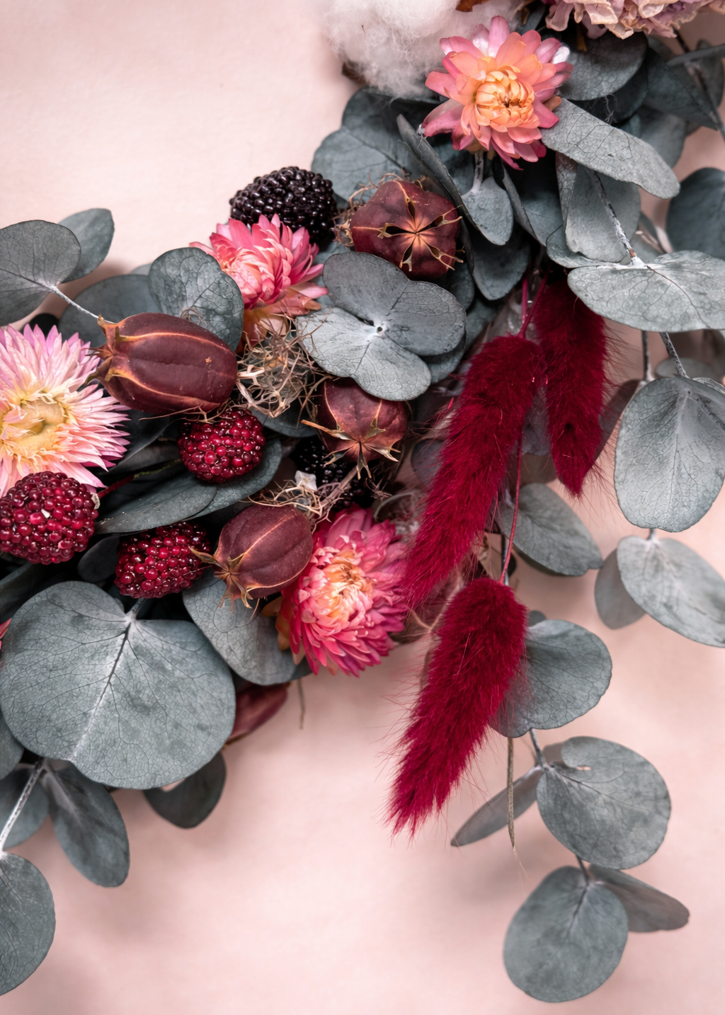 Floral arrangement with pink flowers, red berries, and eucalyptus leaves on a soft pink background