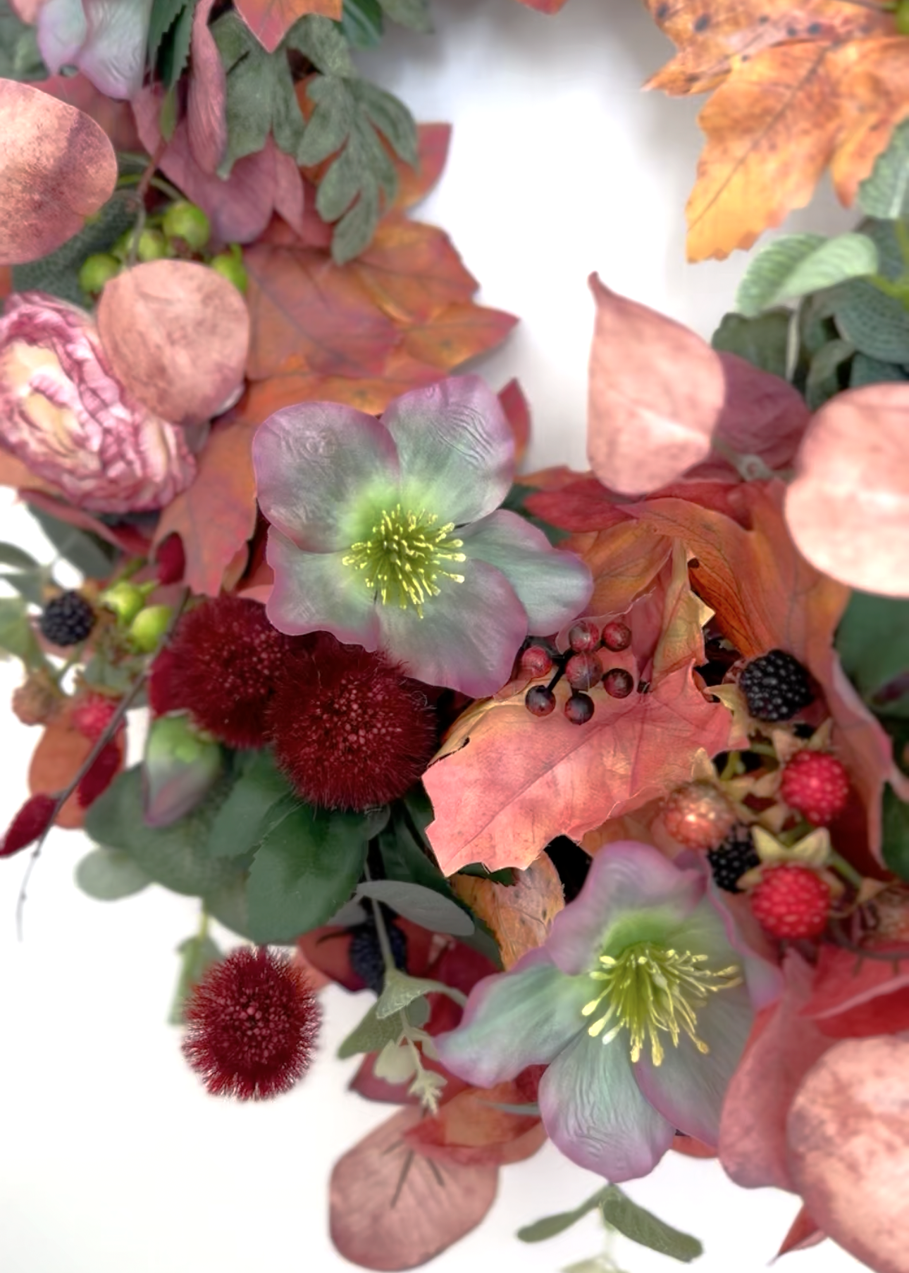 An autumn floral wreath featuring pale green hollyhocks with yellow centers, burgundy pom-pom flowers, pink peonies, and orange-brown leaves on a white background.