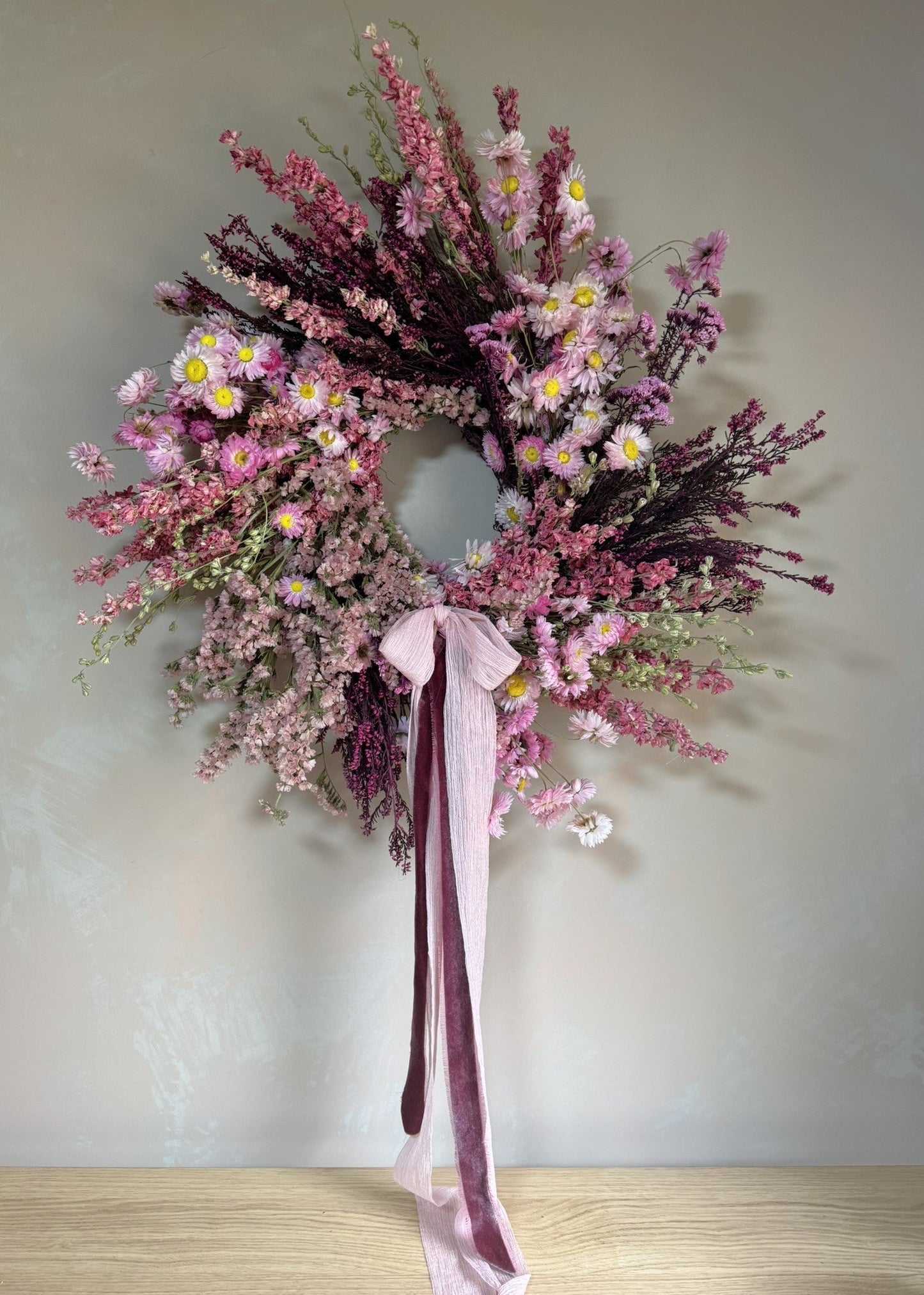 Floral wreath with pink and purple flowers and a ribbon on a plain background