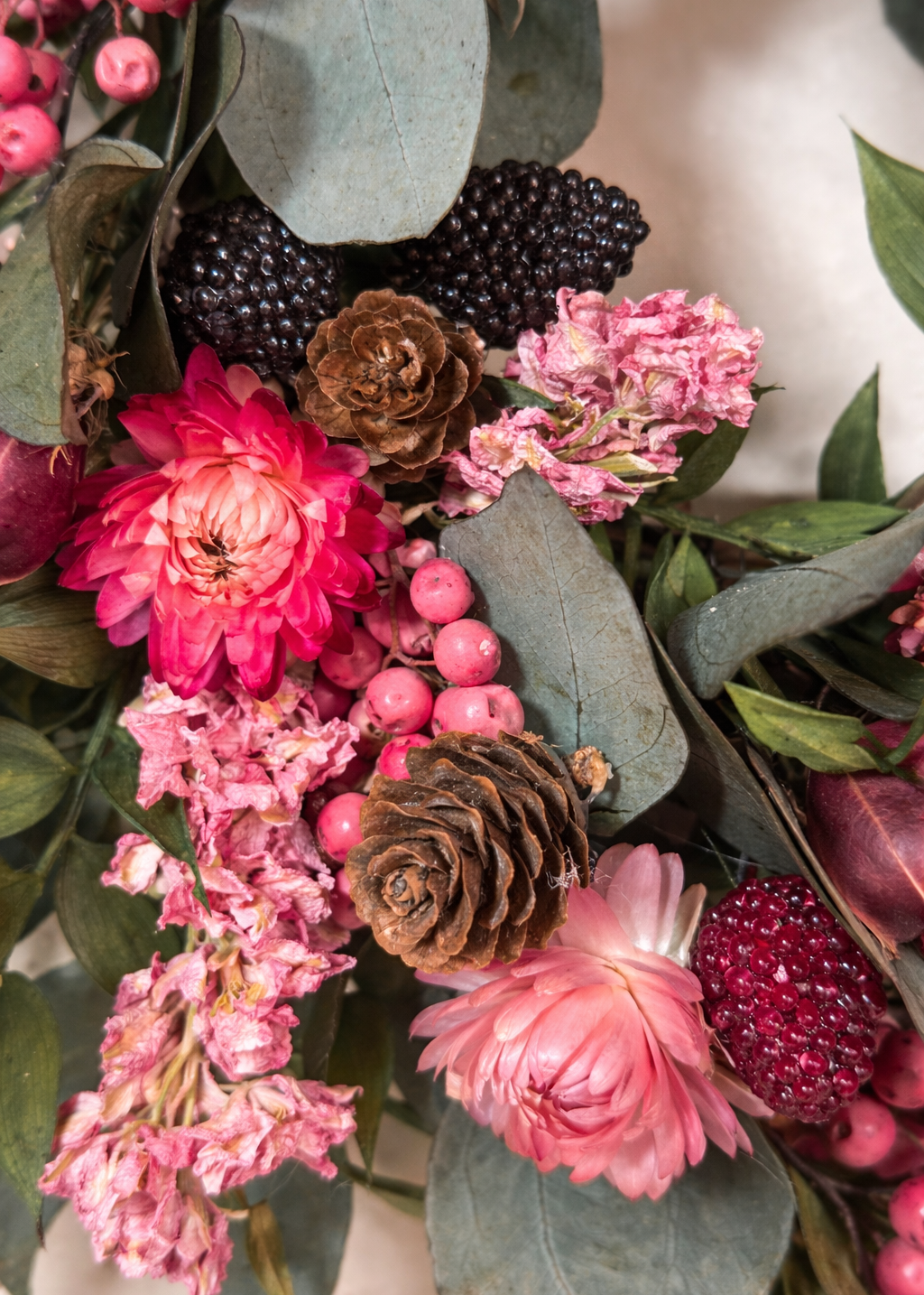 Bouquet of pink flowers, green leaves, and pinecones on a light background