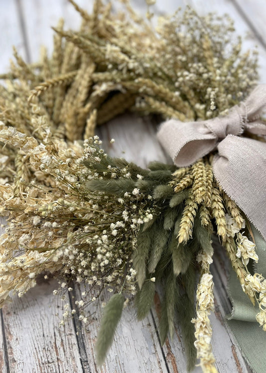 Wreath made of dried flowers and herbs with a soft bow on a wooden surface