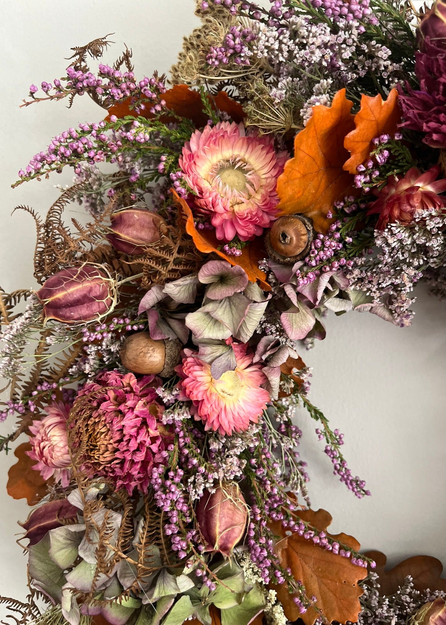 Decorative floral wreath with pink flowers, green leaves, and brown leaves on a white background