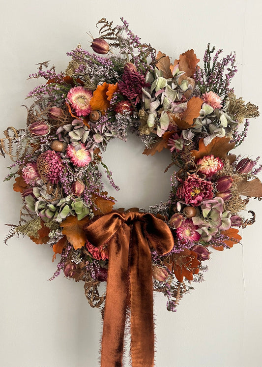 Decorative wreath with autumnal flowers and a brown ribbon on a white background