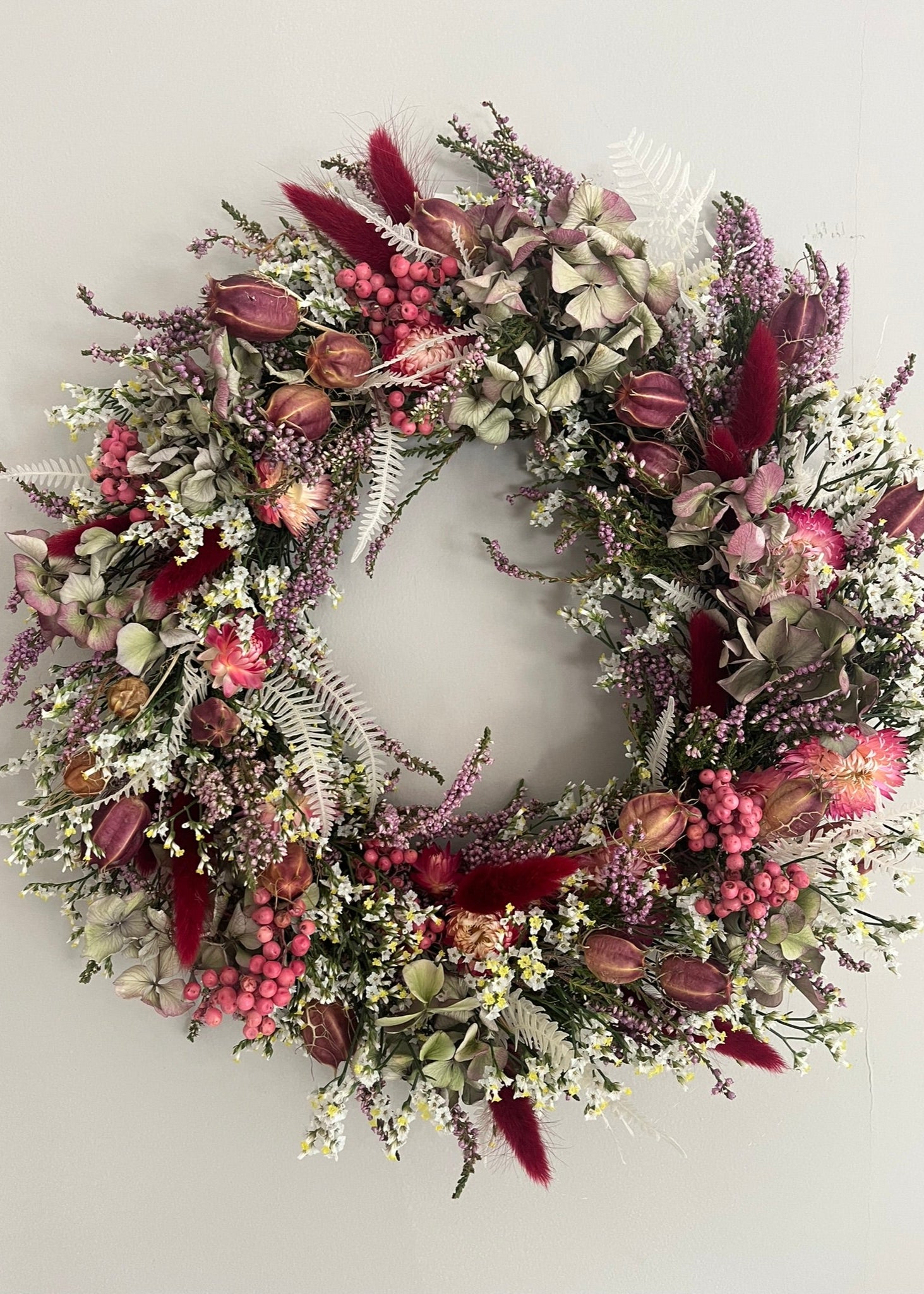 pretty autumnal dried flower wreath in shades of burgundy, red, green, white for a wall or door