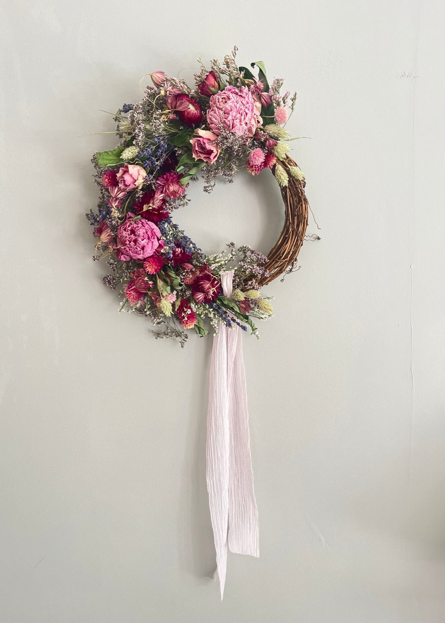 Floral wreath with pink flowers and a white ribbon on a light gray background
