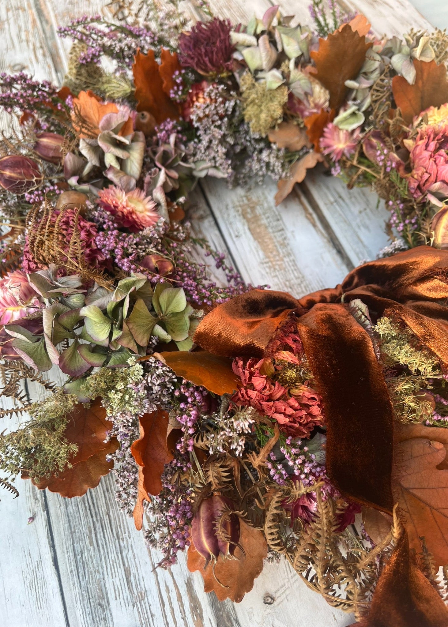 Autumn-themed wreath with dried flowers and leaves on a wooden surface