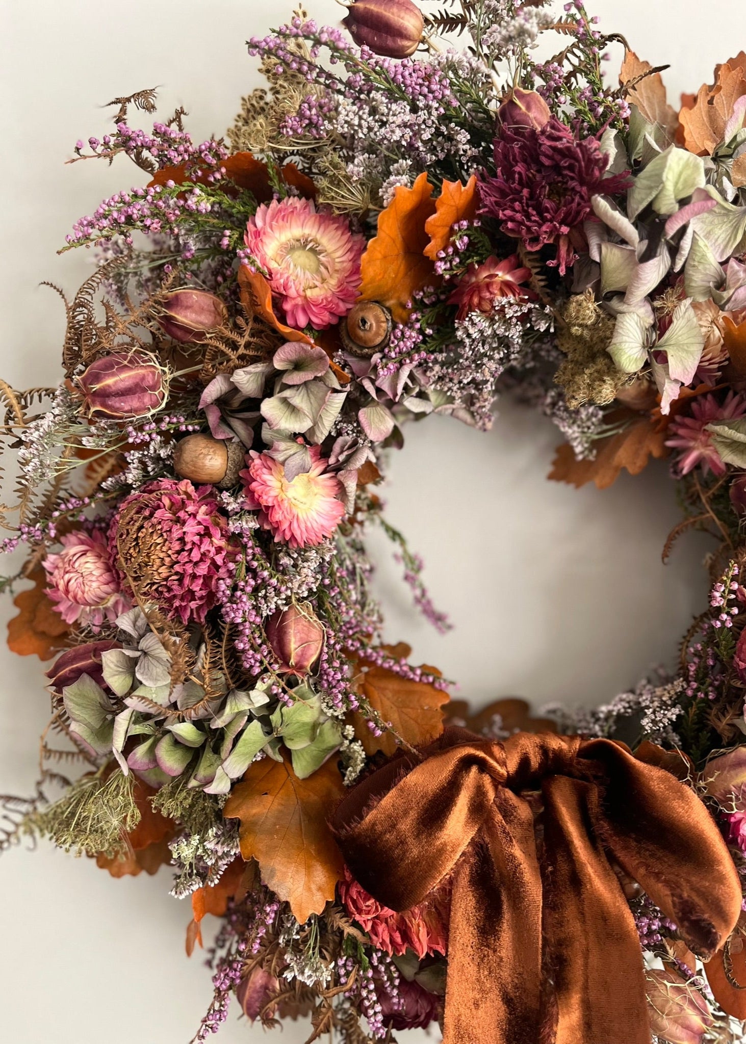 Decorative wreath with dried flowers and a brown ribbon on a white background