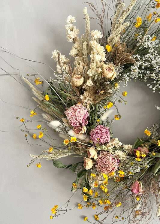 Floral wreath with dried flowers and pink artificial flowers on a light gray background