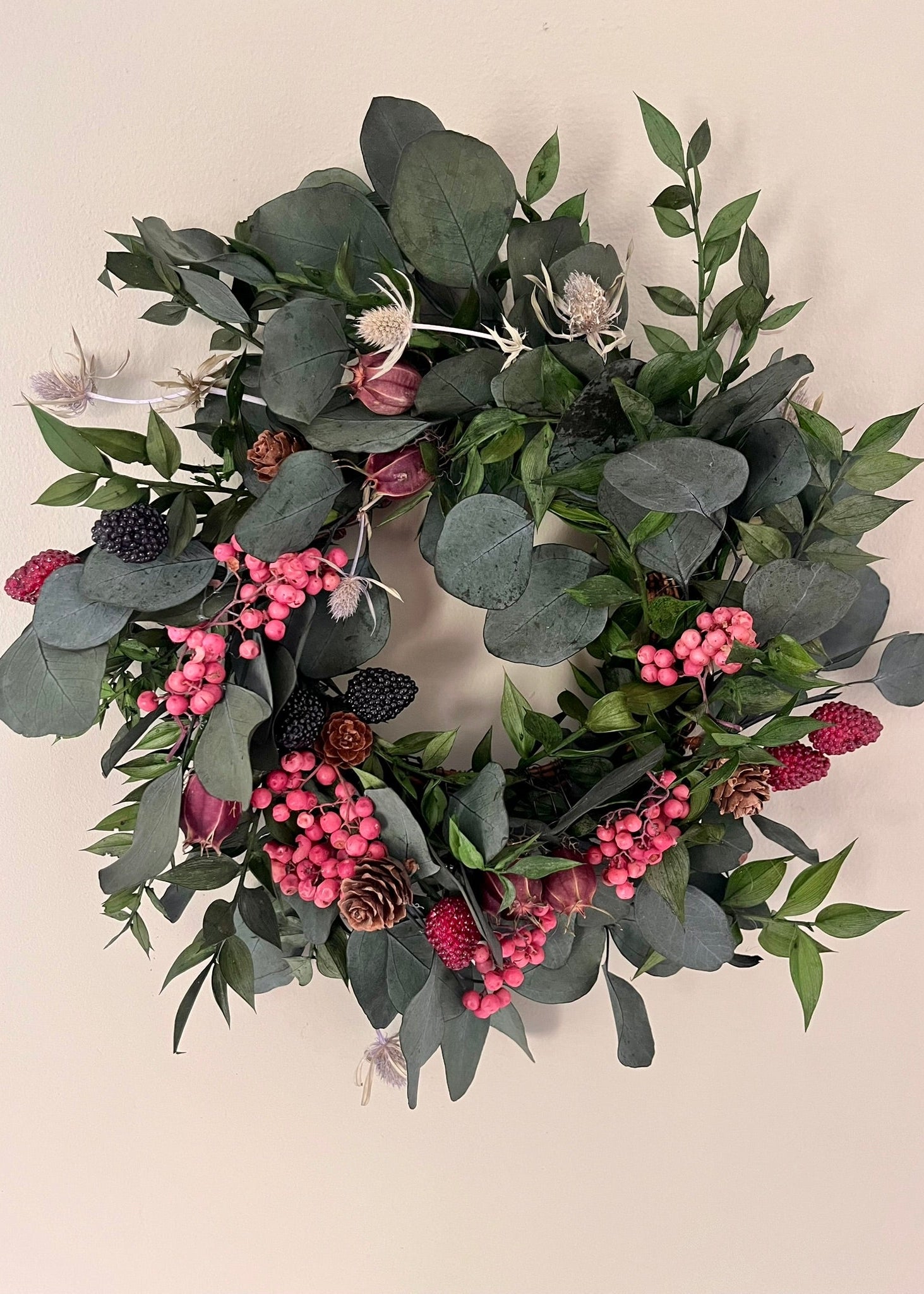 Decorative wreath with green leaves and pink berries on a beige background