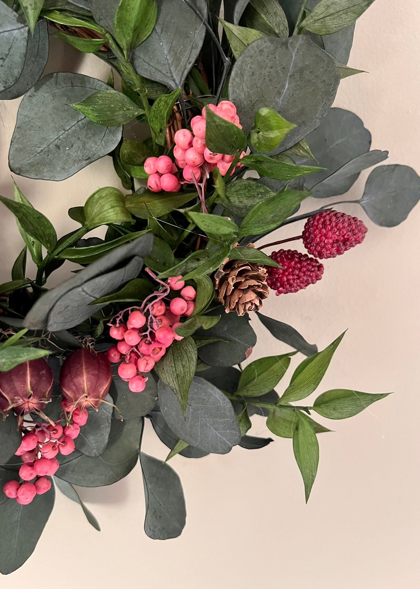 Decorative arrangement of green leaves, pink berries, and pine cones on a beige background