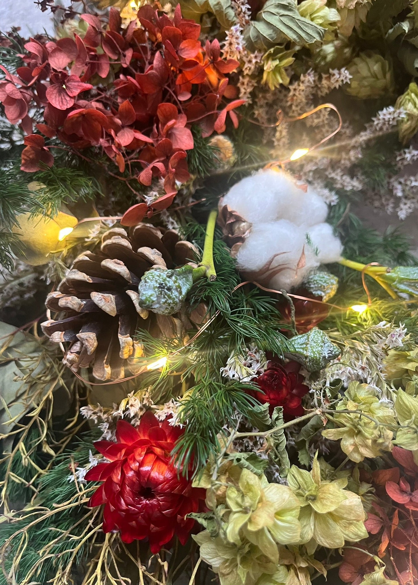 Decorative wreath with pine cones, flowers, and lights on a green background