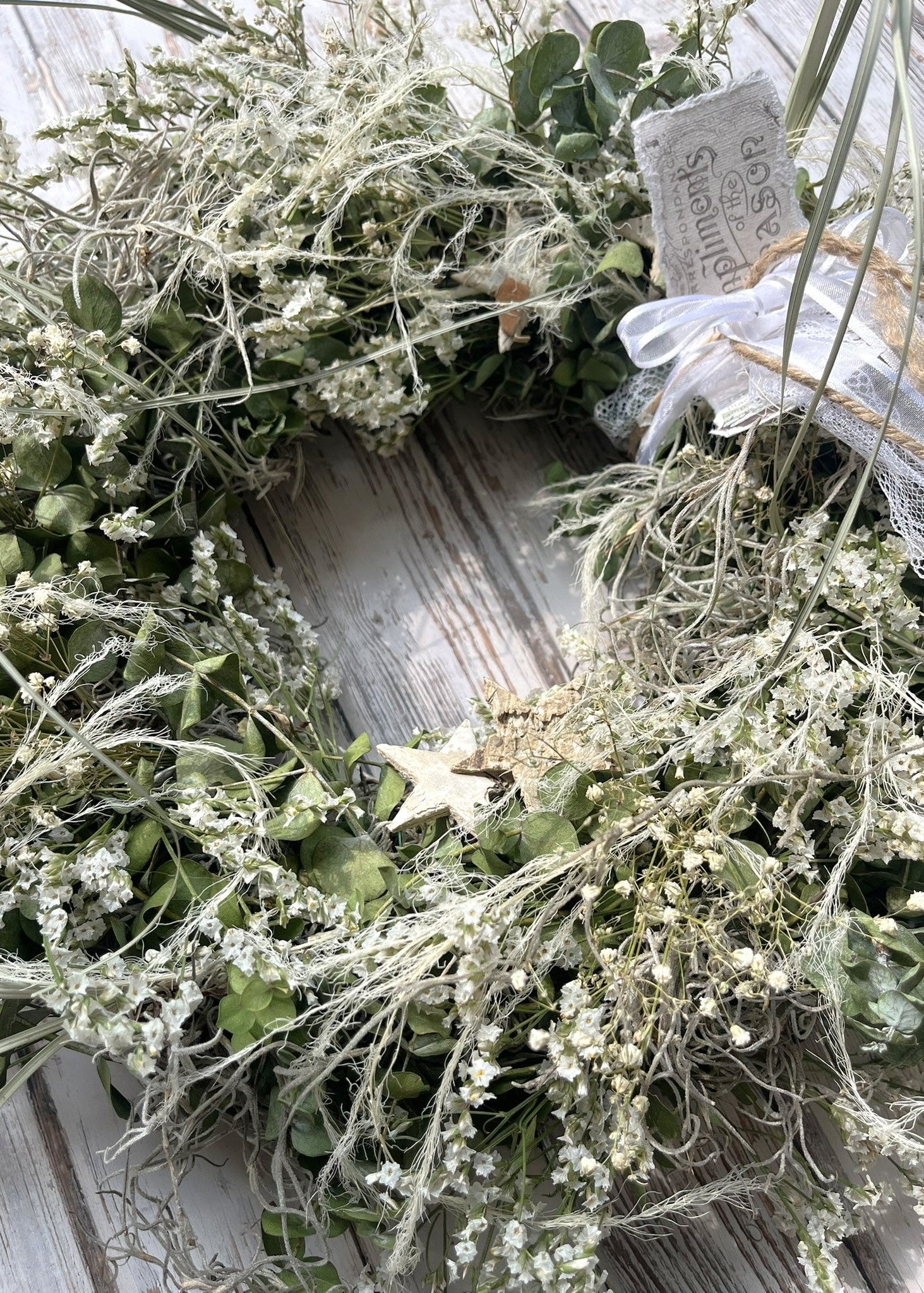 Decorative wreath with greenery and a white label on a wooden surface