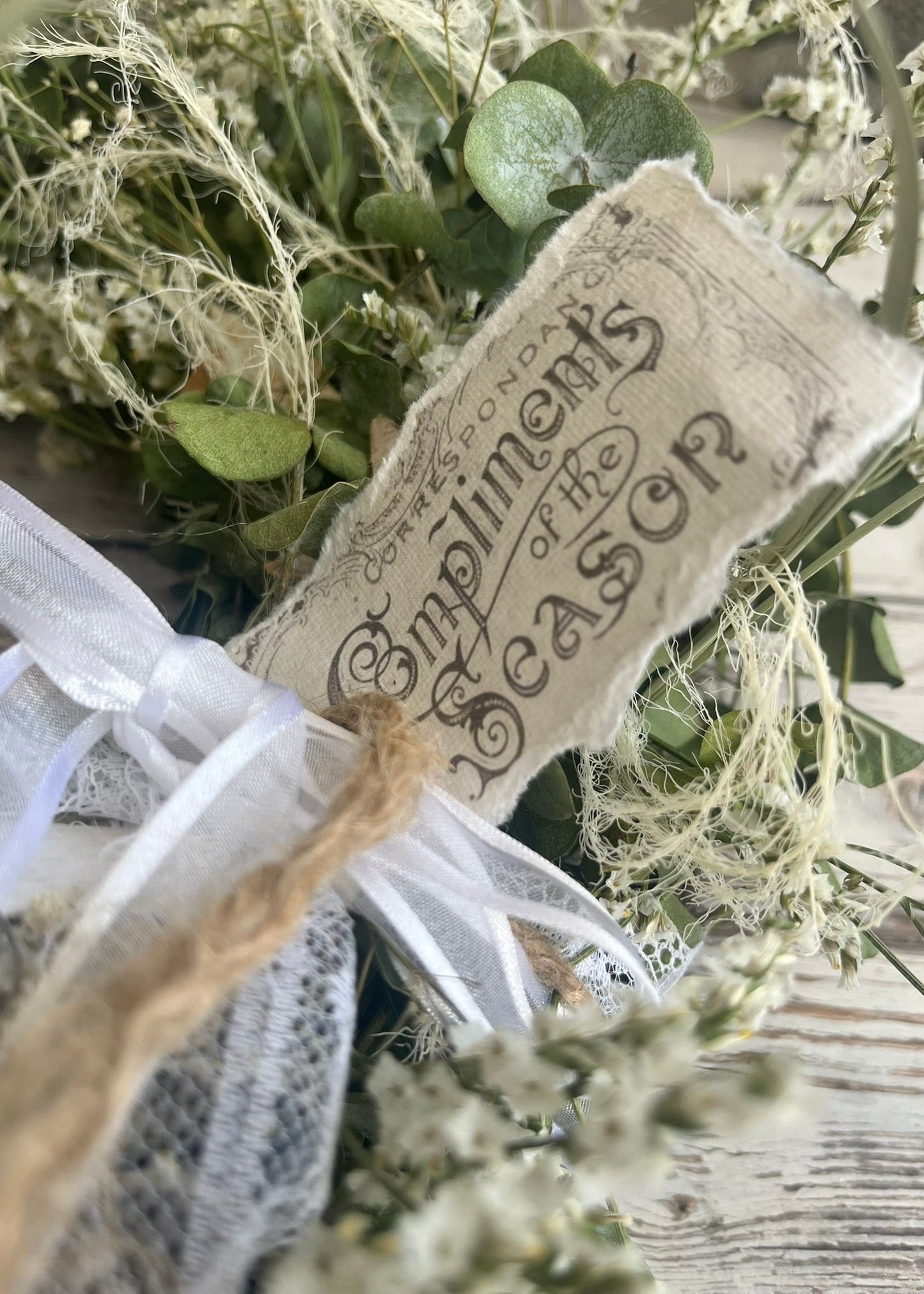 Decorative sign with text on a wreath with greenery and white ribbons.