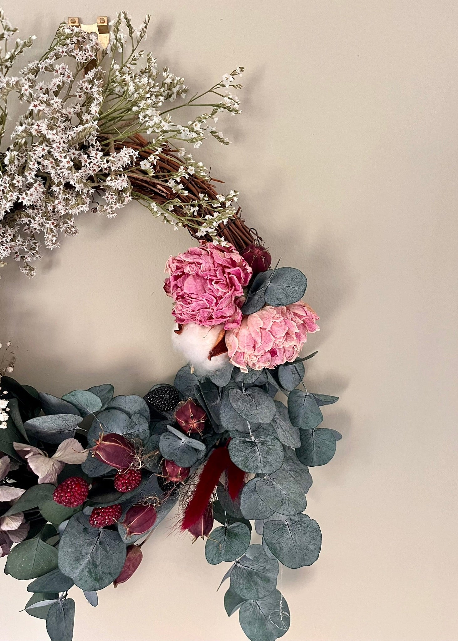 Decorative wreath with pink flowers, green leaves, and red berries on a neutral background