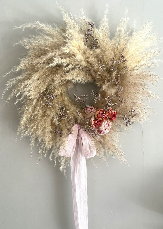 Decorative wreath with pampas grass, pink ribbon, and red flowers on a plain background