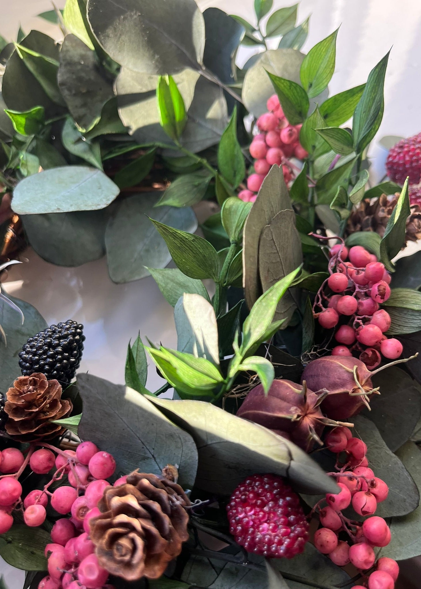 Decorative arrangement of green leaves, pink berries, and pinecones on a white background