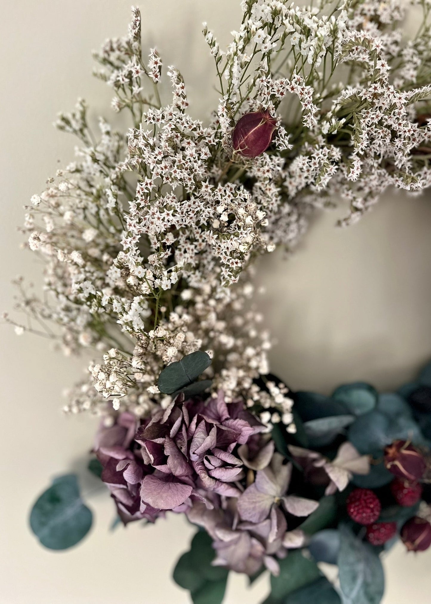 Close-up of a floral arrangement with white flowers, purple hydrangeas, and green leaves on a light background.