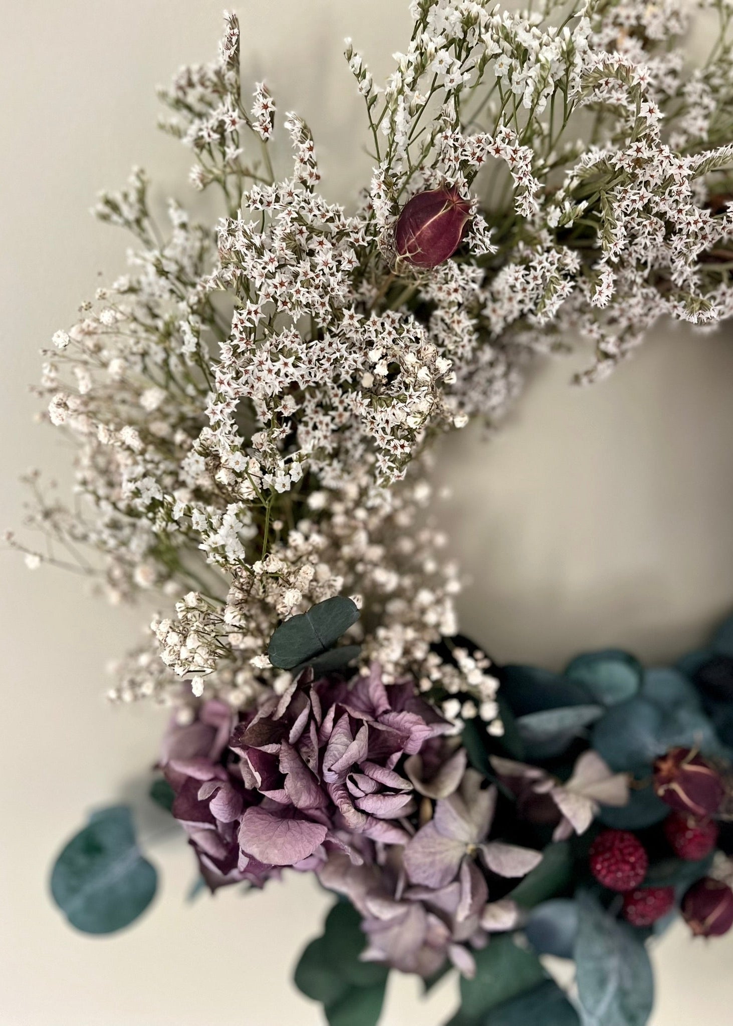 Close-up of a floral arrangement with white flowers, purple hydrangeas, and green leaves on a light background.