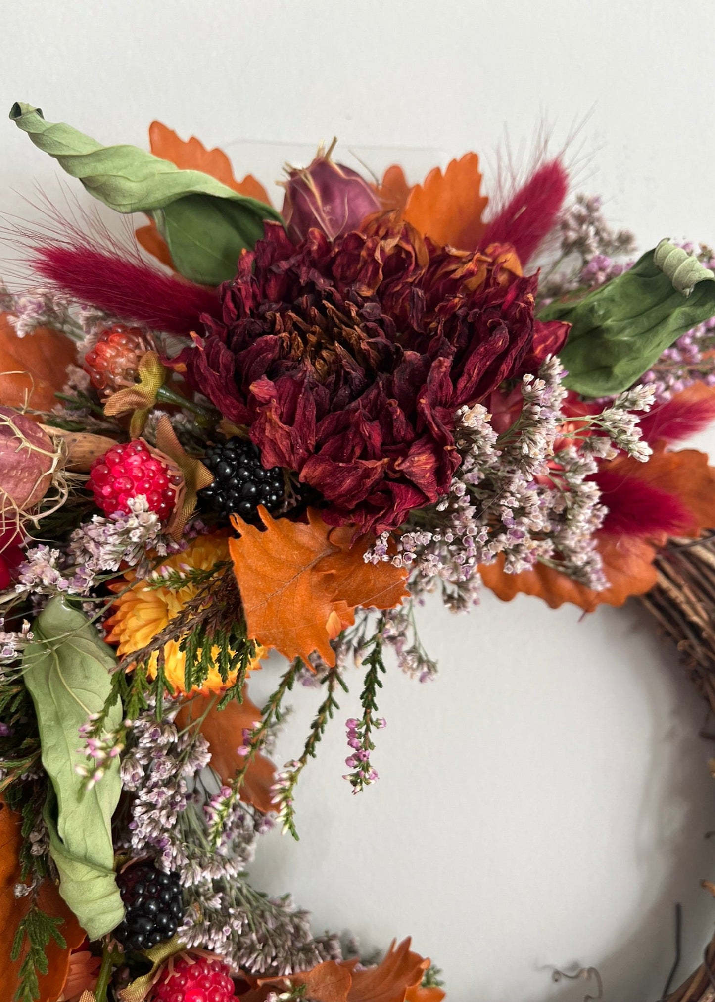 Autumn-themed floral arrangement with dried flowers, leaves, and berries on a white background