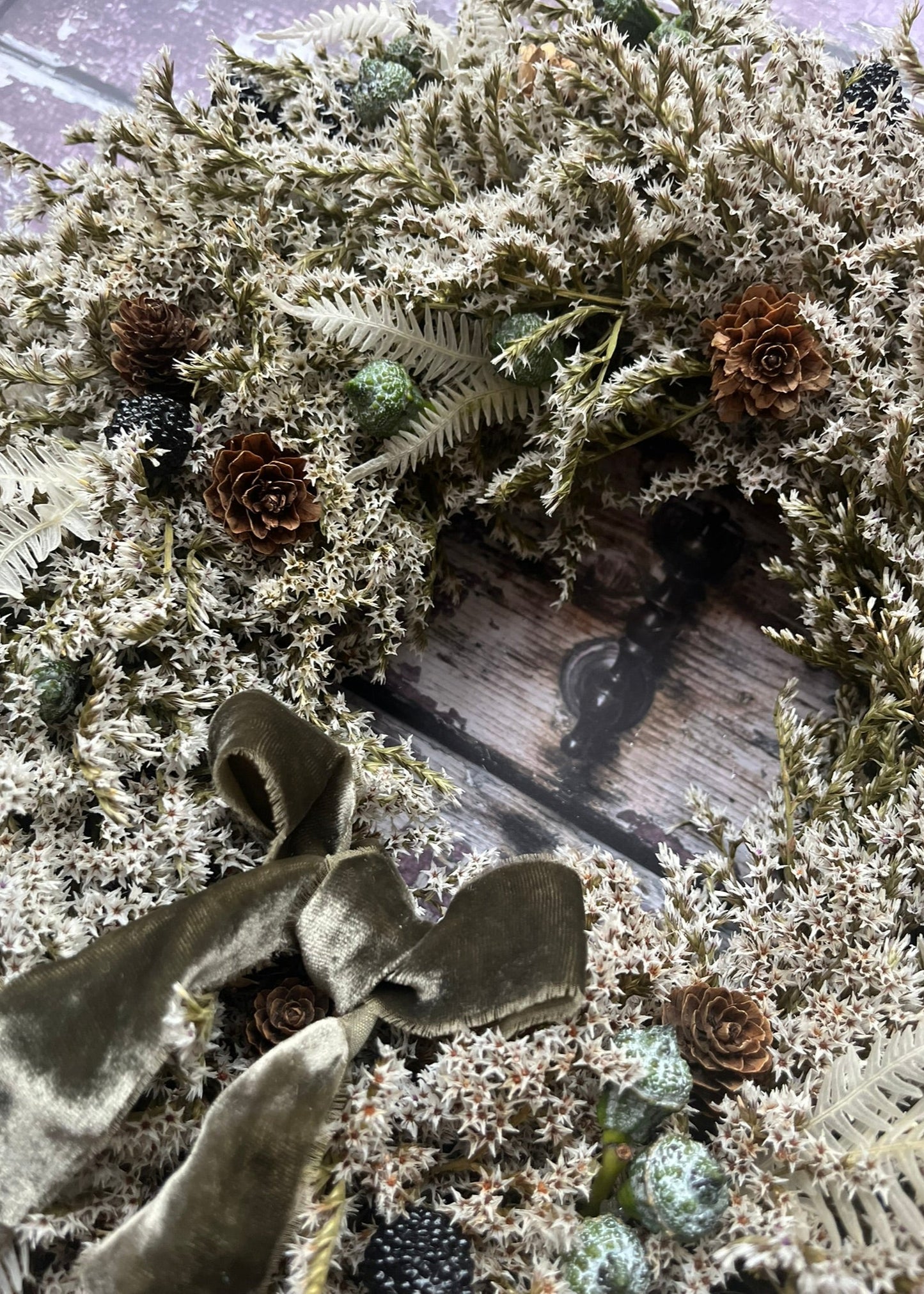 Decorative wreath with greenery, pinecones, and ribbons on a wooden surface