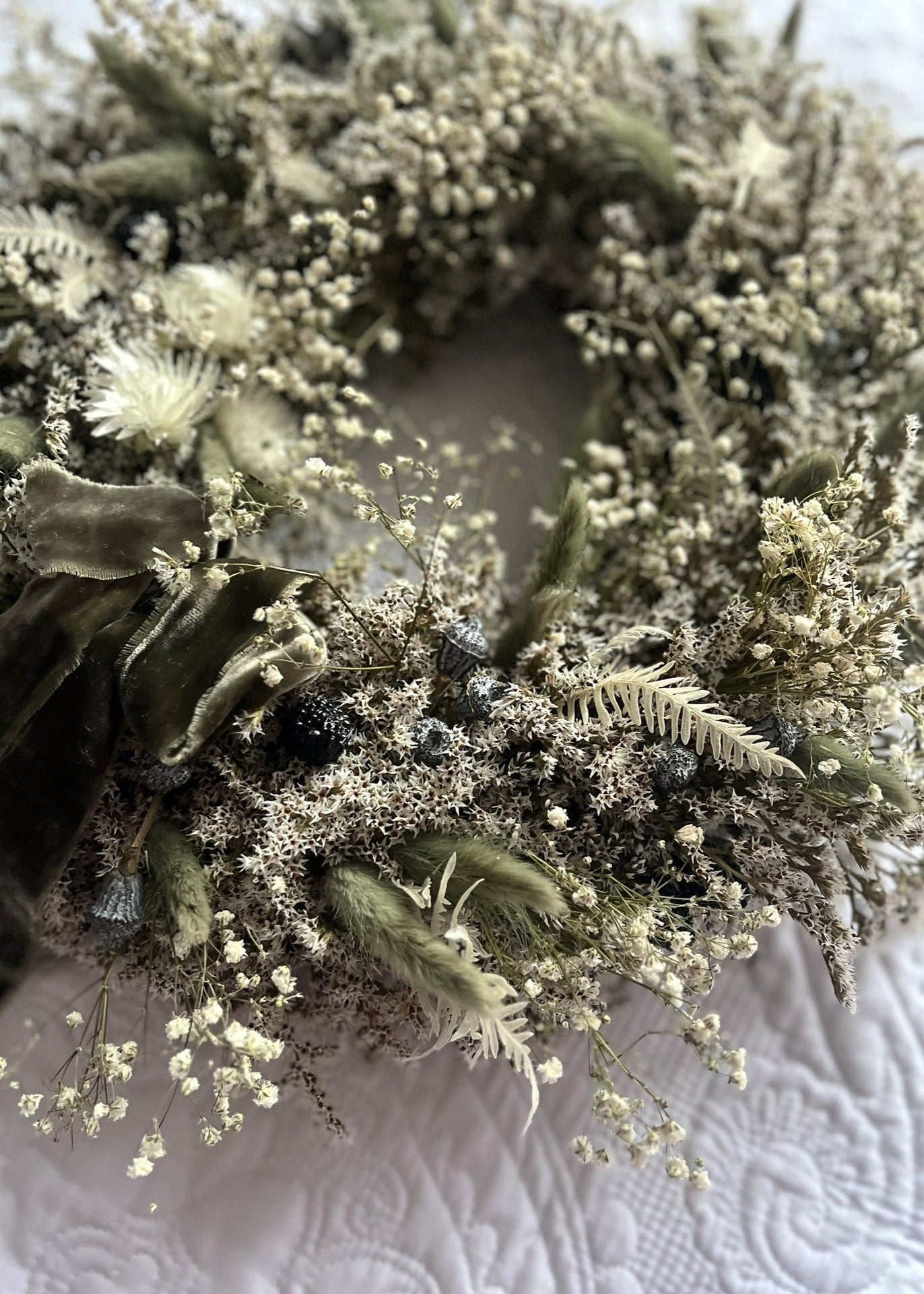 Close-up of a floral wreath with greenery and small white flowers on a textured surface.