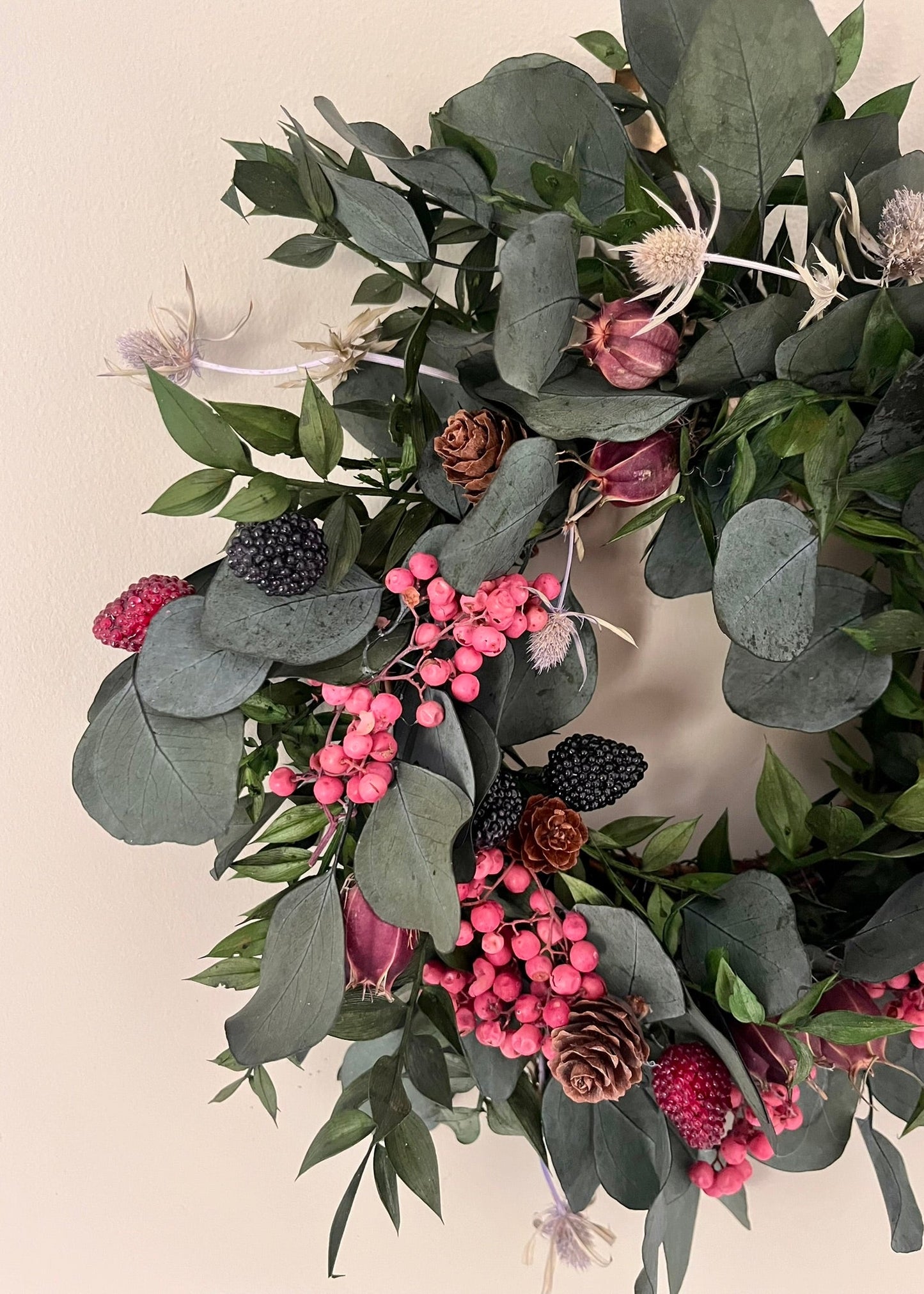 Decorative wreath with green leaves, pink berries, and other elements on a beige background