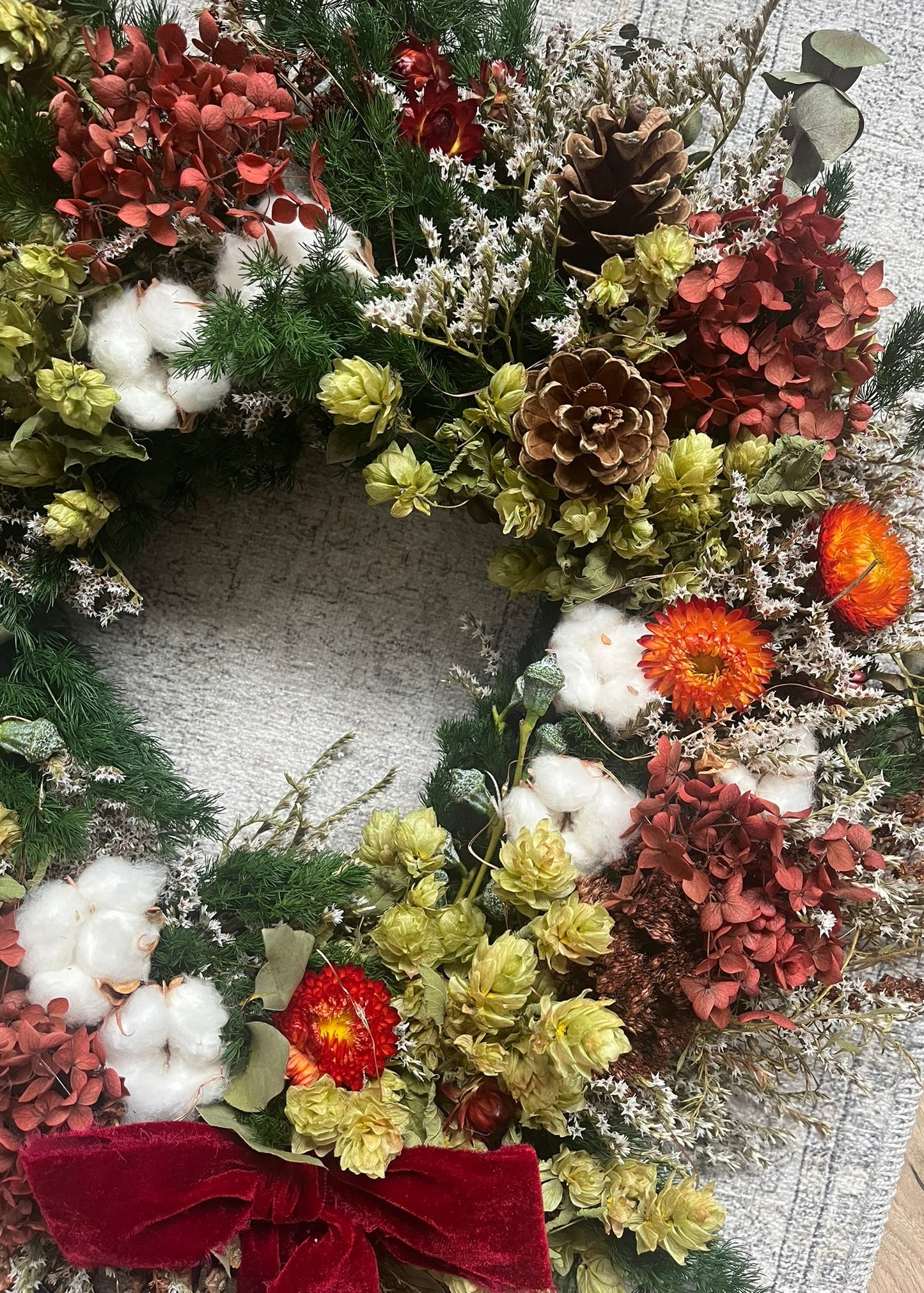 Decorative wreath with flowers, pinecones, and cotton on a textured surface