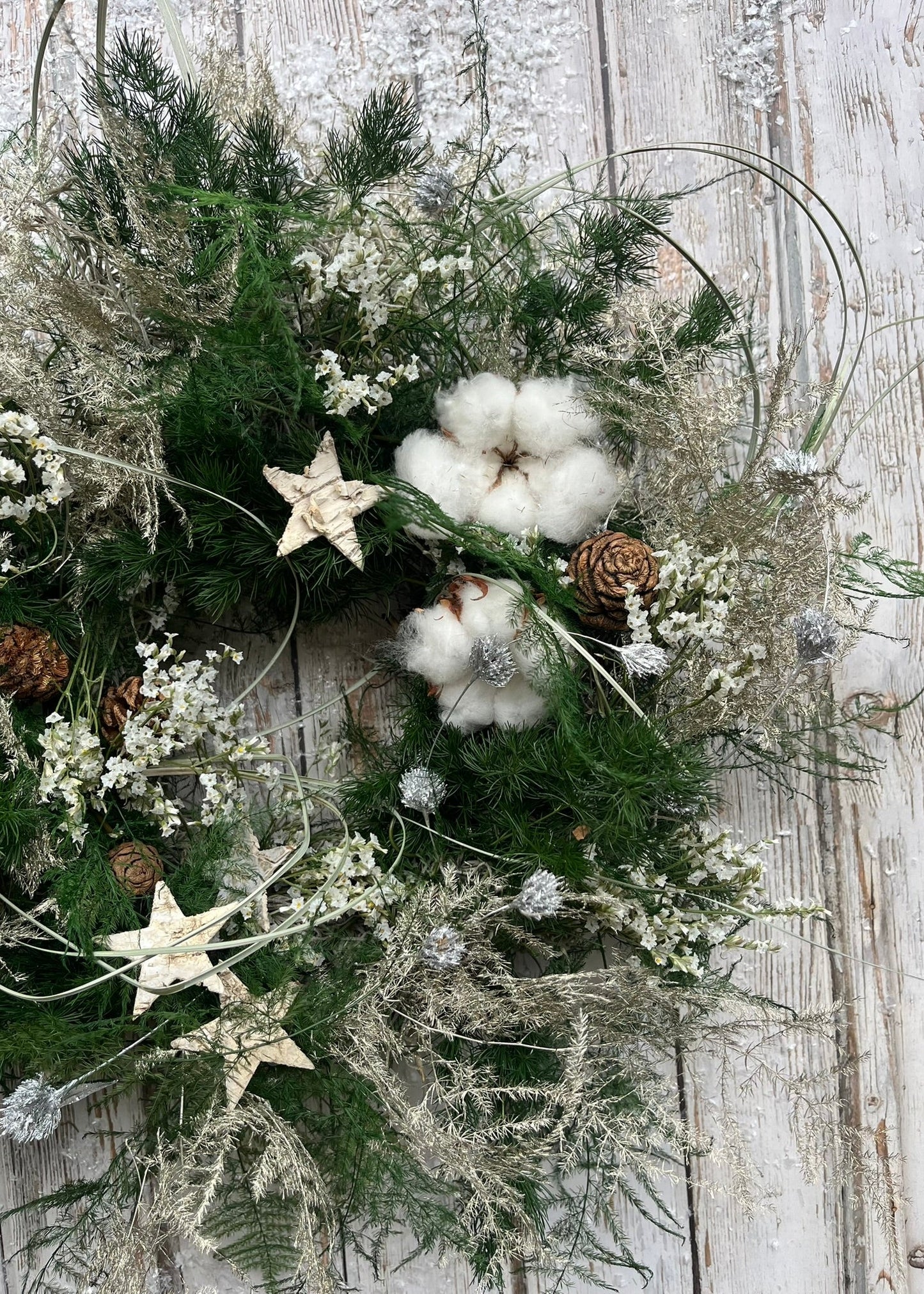 Decorative wreath with greenery, cotton, stars, and pinecones on a wooden surface