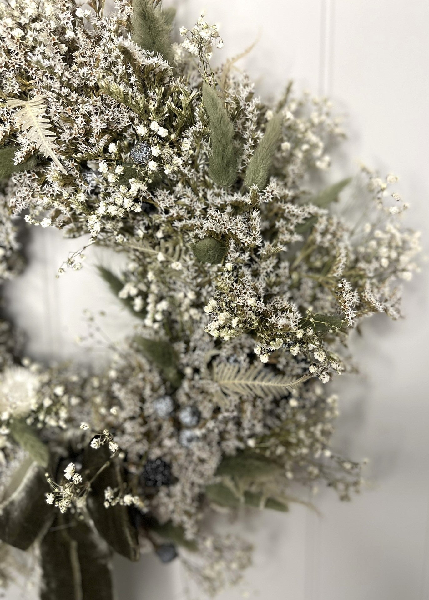 Decorative wreath with greenery and small white flowers on a plain background