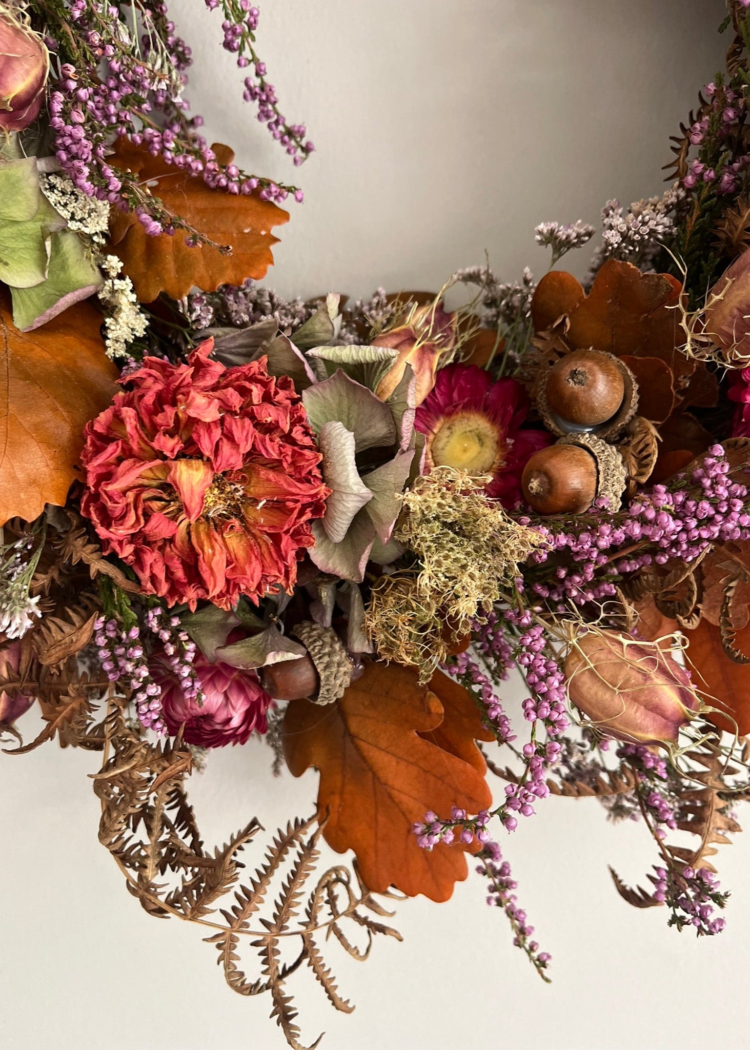 Decorative wreath with autumnal elements including leaves, berries, and flowers on a neutral background.