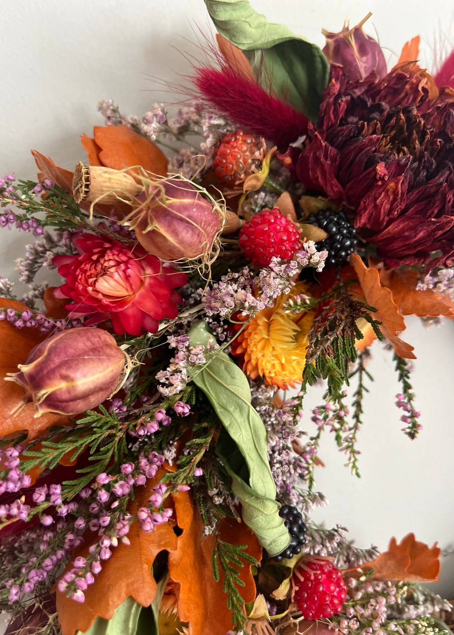 Autumn-themed wreath with dried flowers, leaves, and berries on a white background
